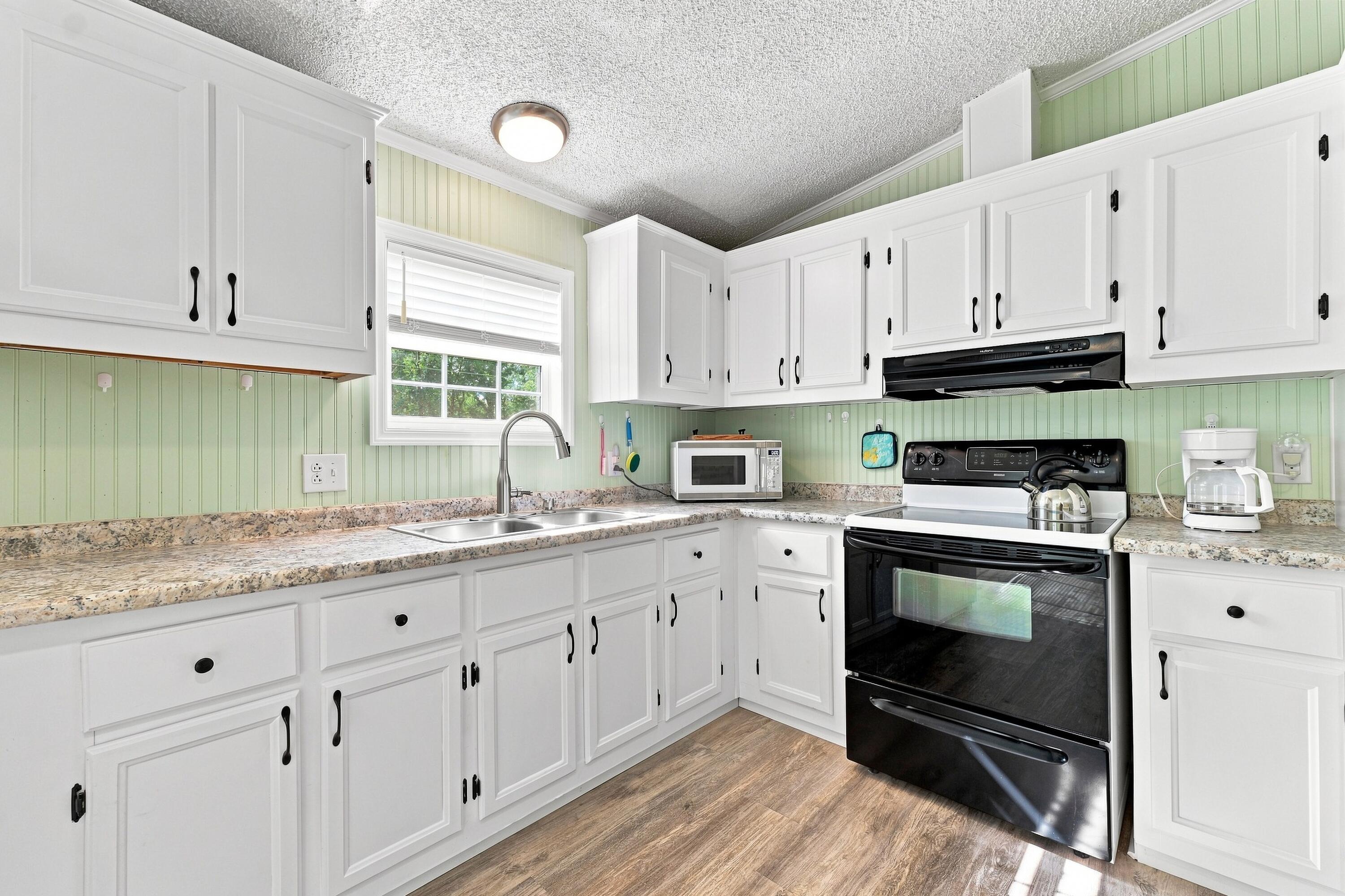 Kitchen with white cabinets, pale green paneling, and a black range beside the sink.