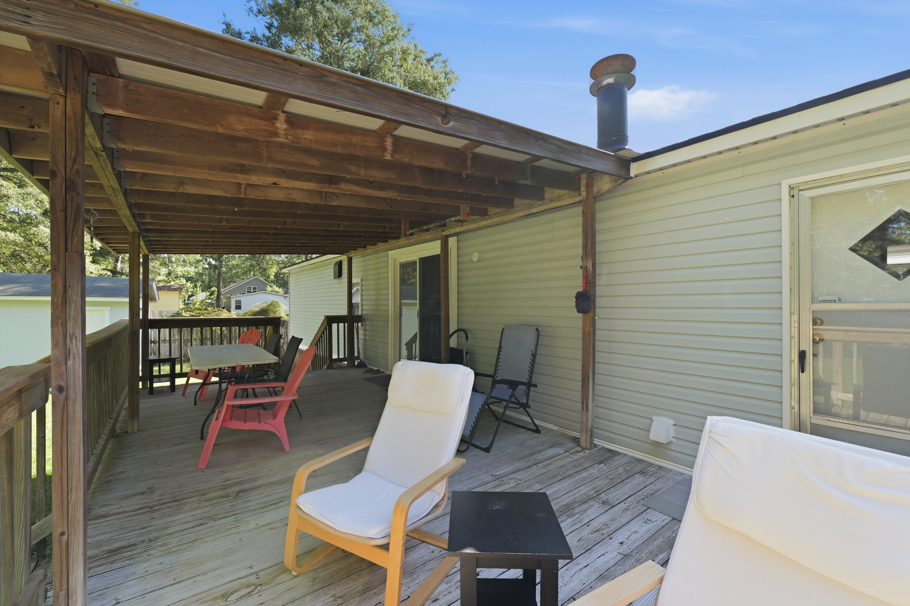 Covered wooden deck with lounge chairs and a dining table beside the home.