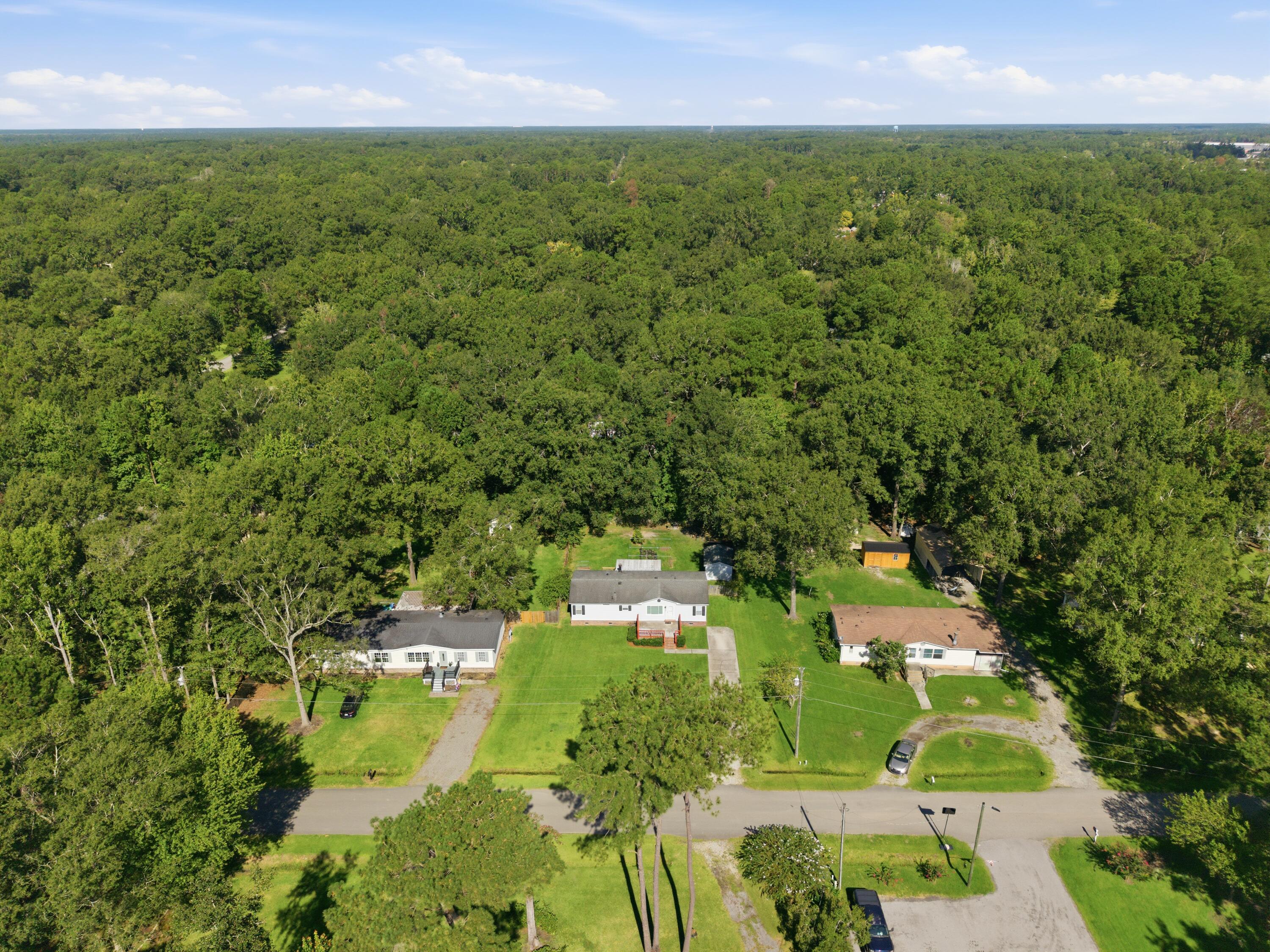 Aerial view of a white house and neighboring homes amid lawns and dense woodland.