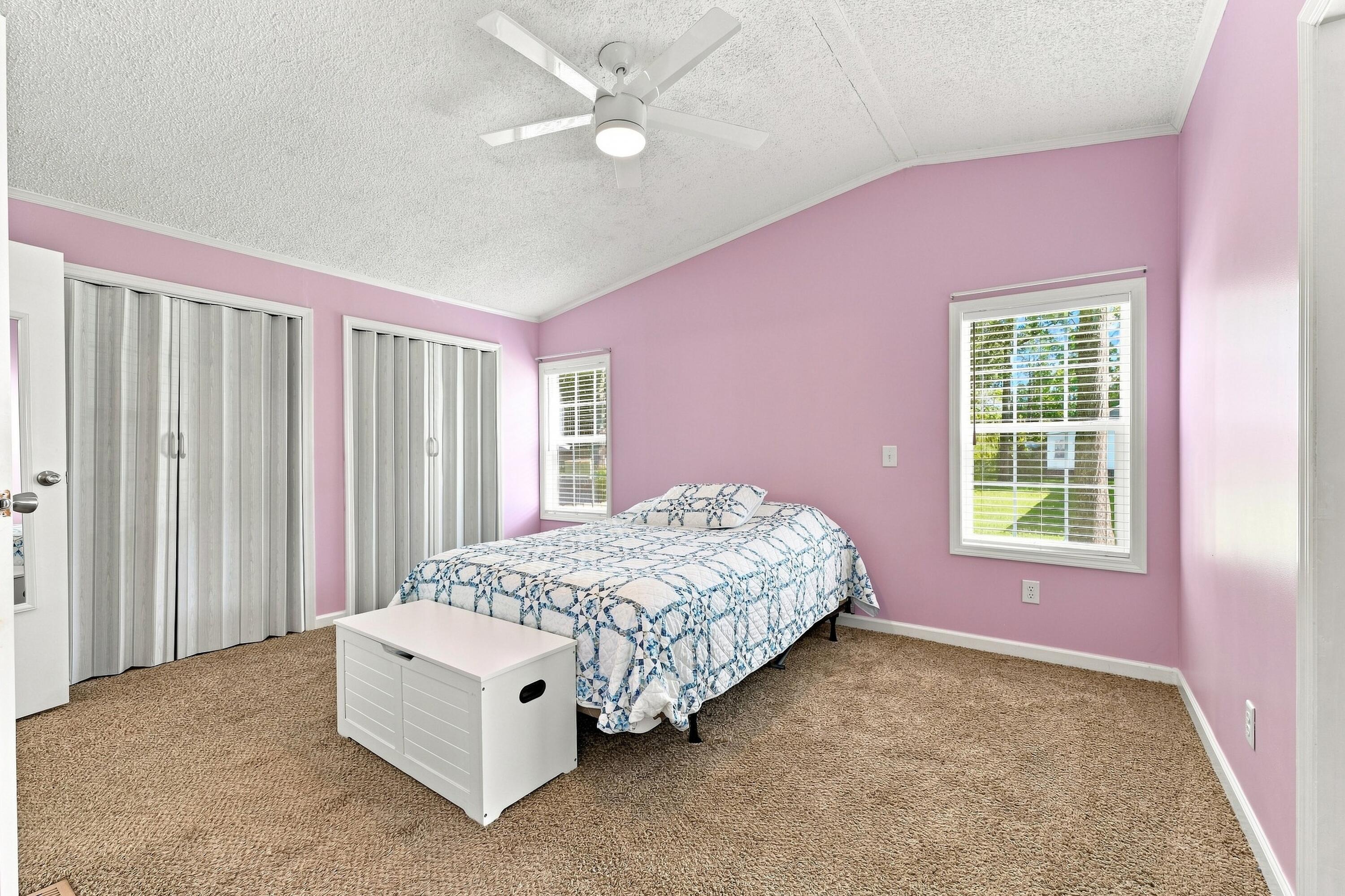 Bedroom with pink walls, a blue-and-white quilt, and windows with white blinds.