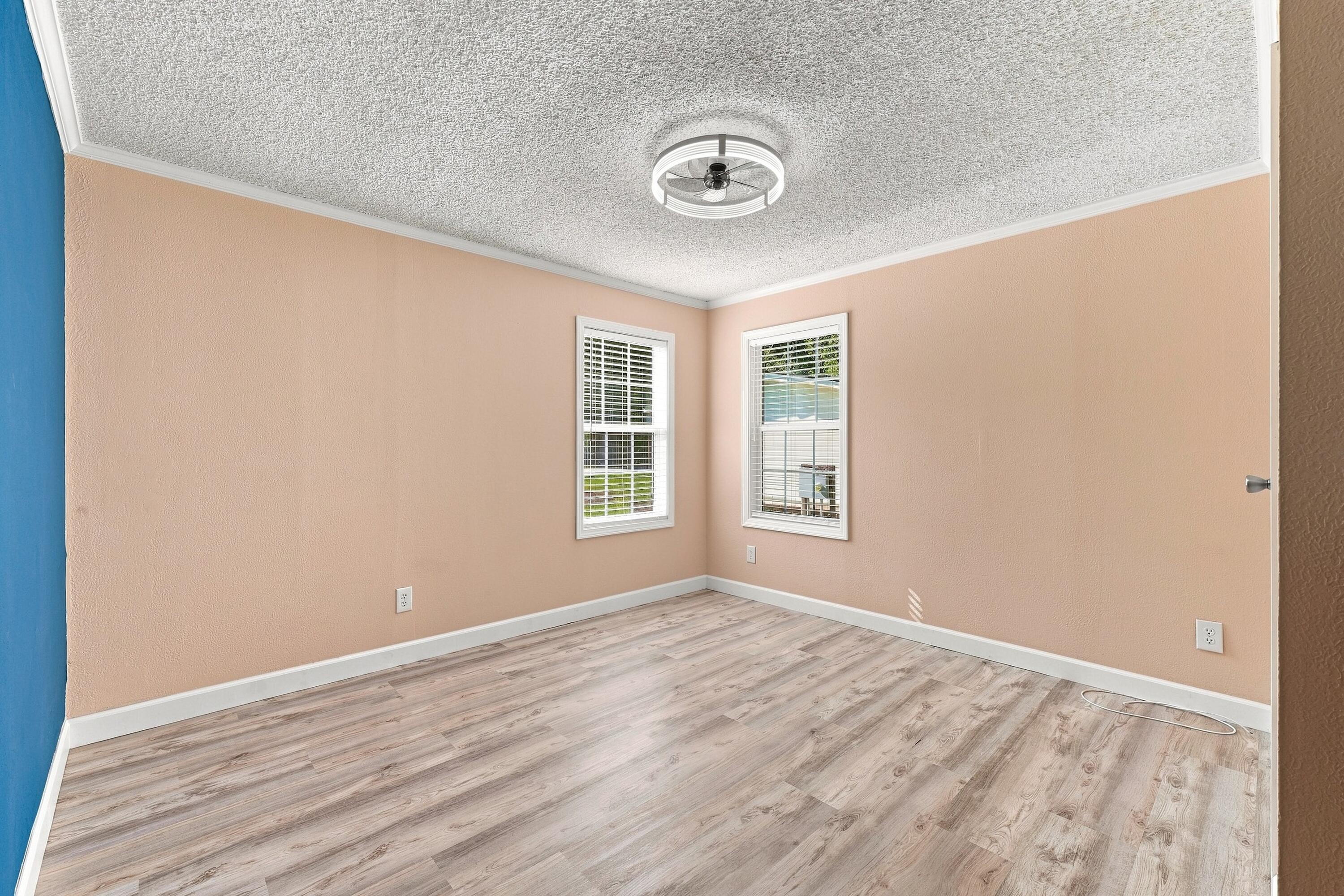 Empty room with peach walls, two windows, gray wood-look flooring, and a ceiling fan.
