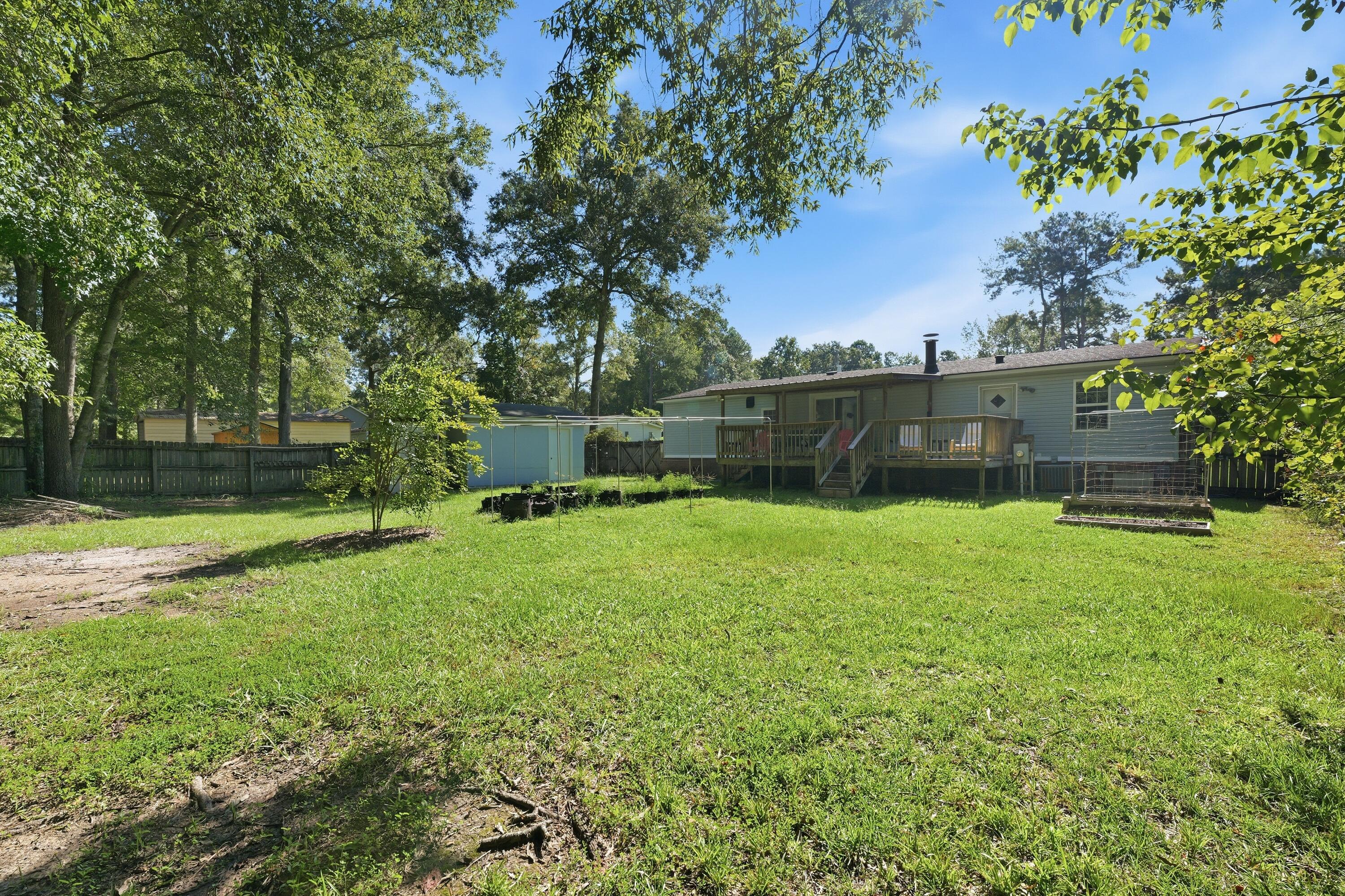 Fenced backyard with a raised wooden deck, broad lawn, mature trees, and a small outbuilding.