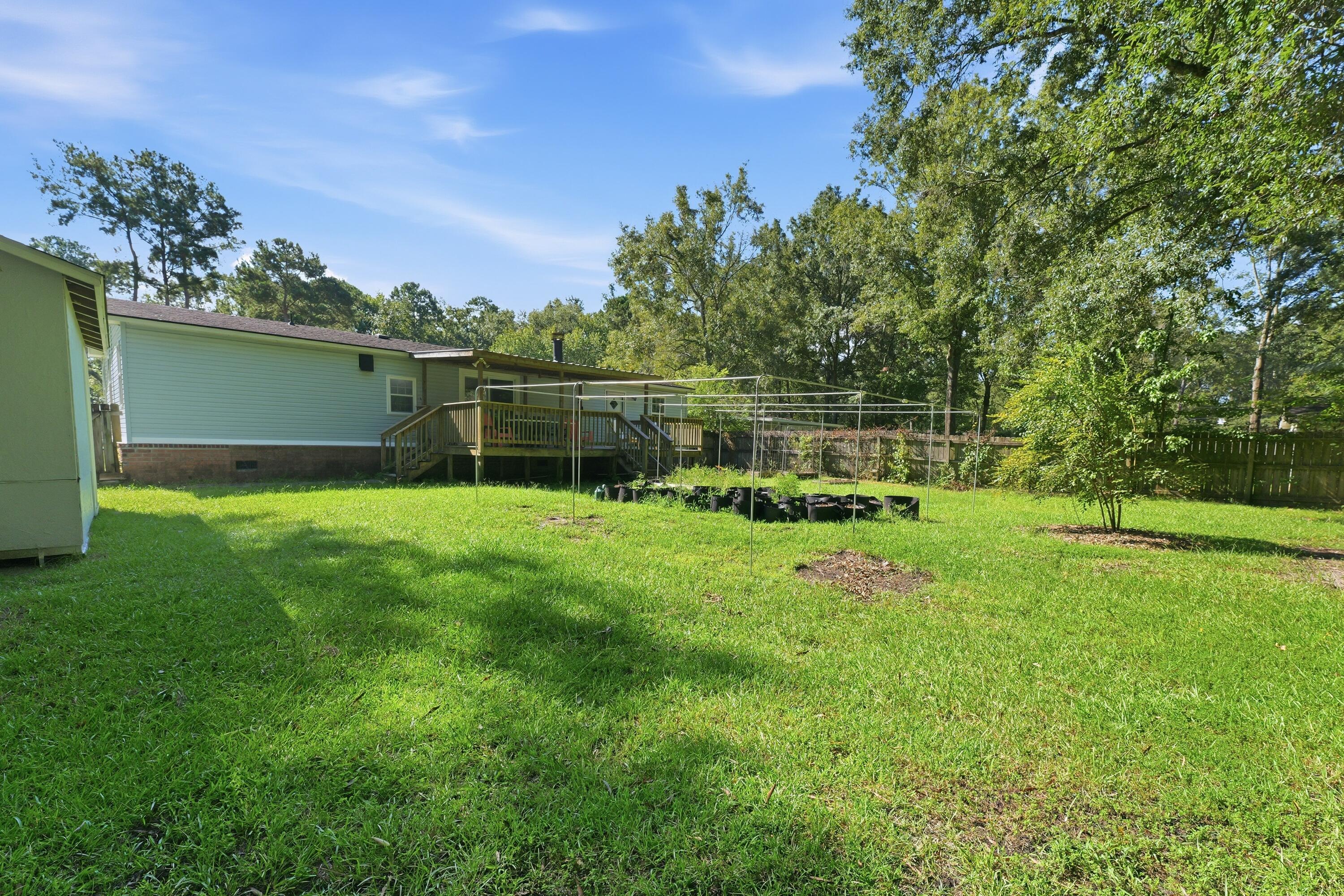 Backyard with a broad lawn, raised wooden deck, garden trellises, and mature trees.