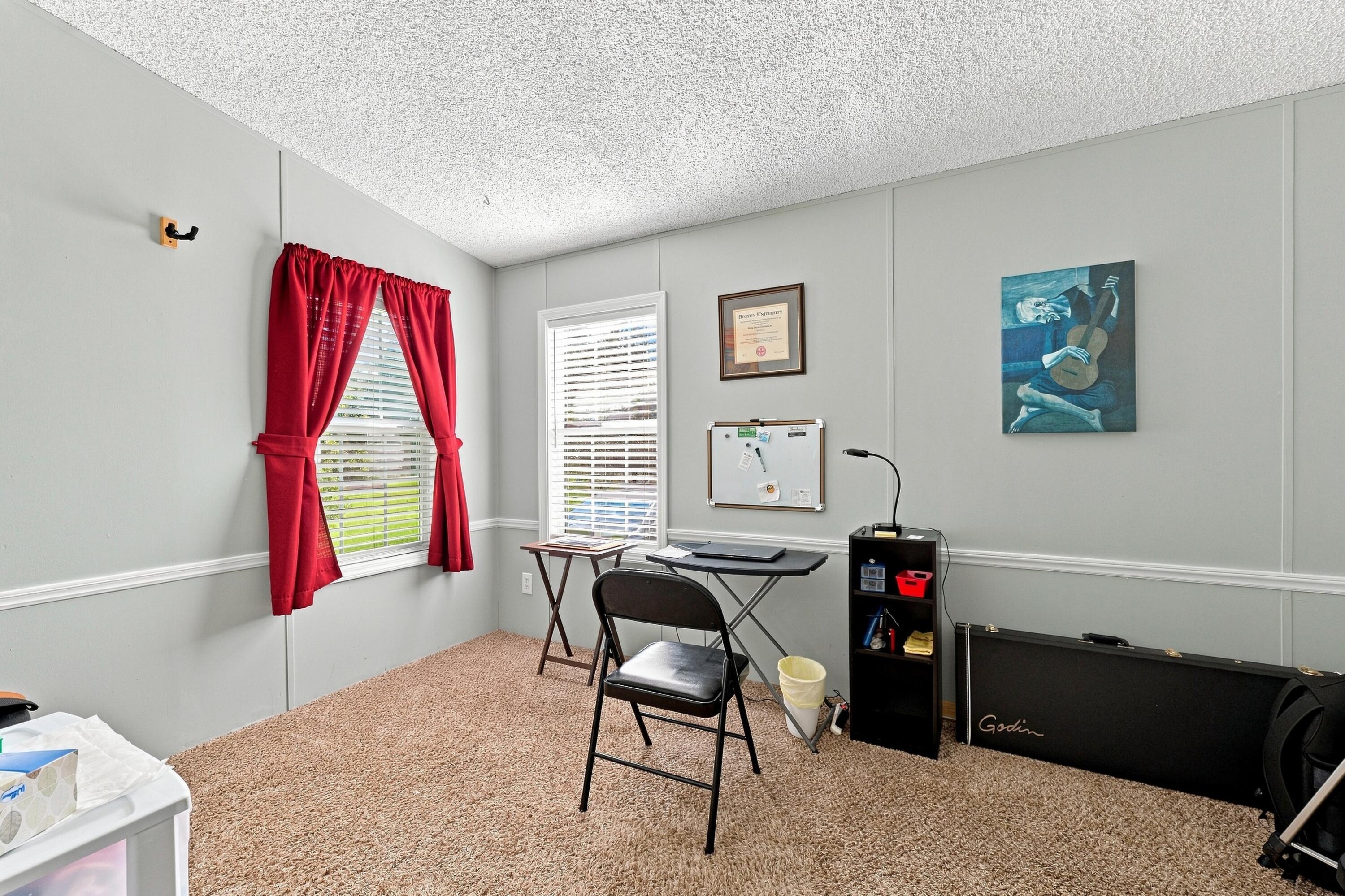 Carpeted home office with red-curtained windows, a folding desk, and a guitar case.