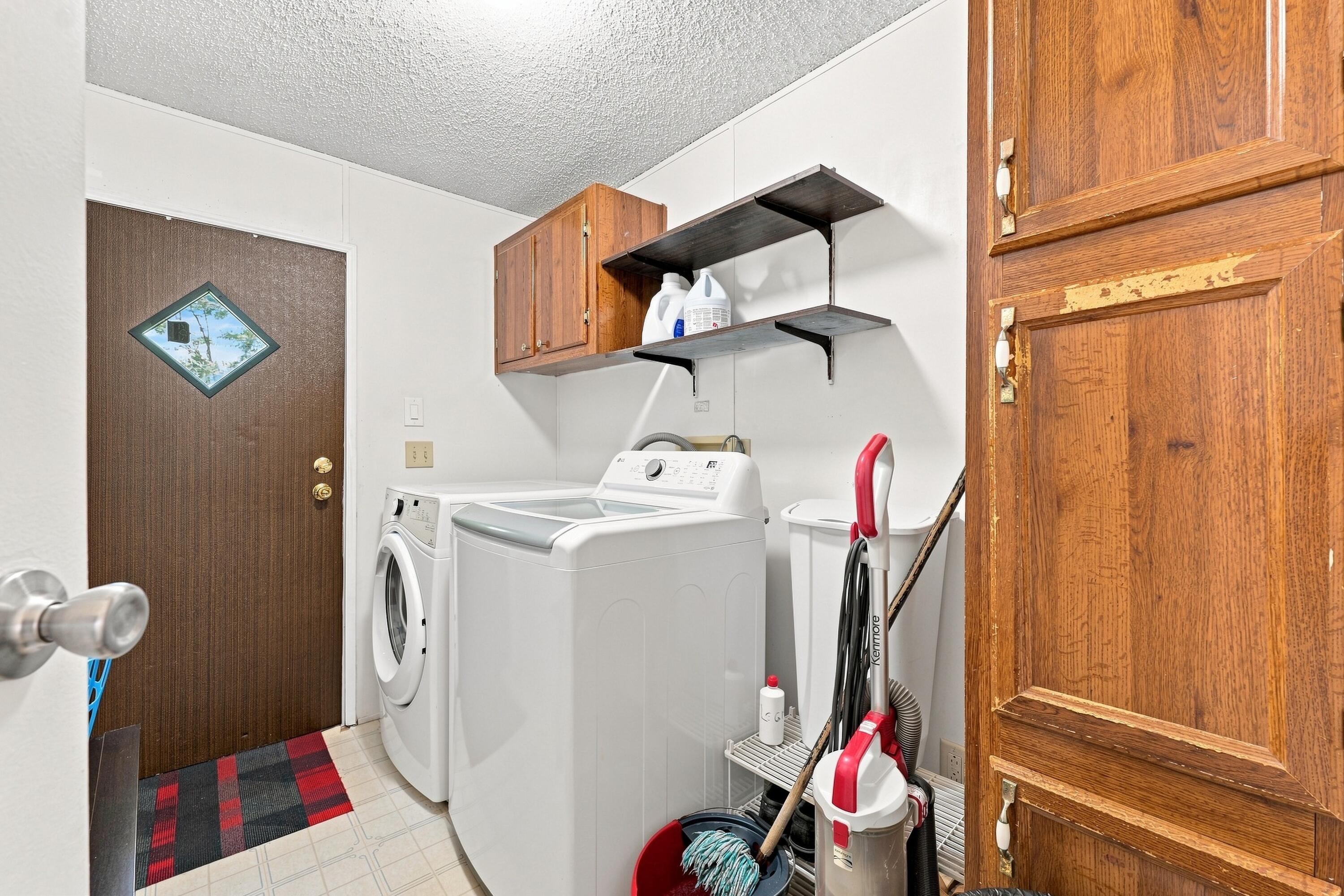 Laundry room with white washer and dryer, wooden cabinets, and cleaning supplies.