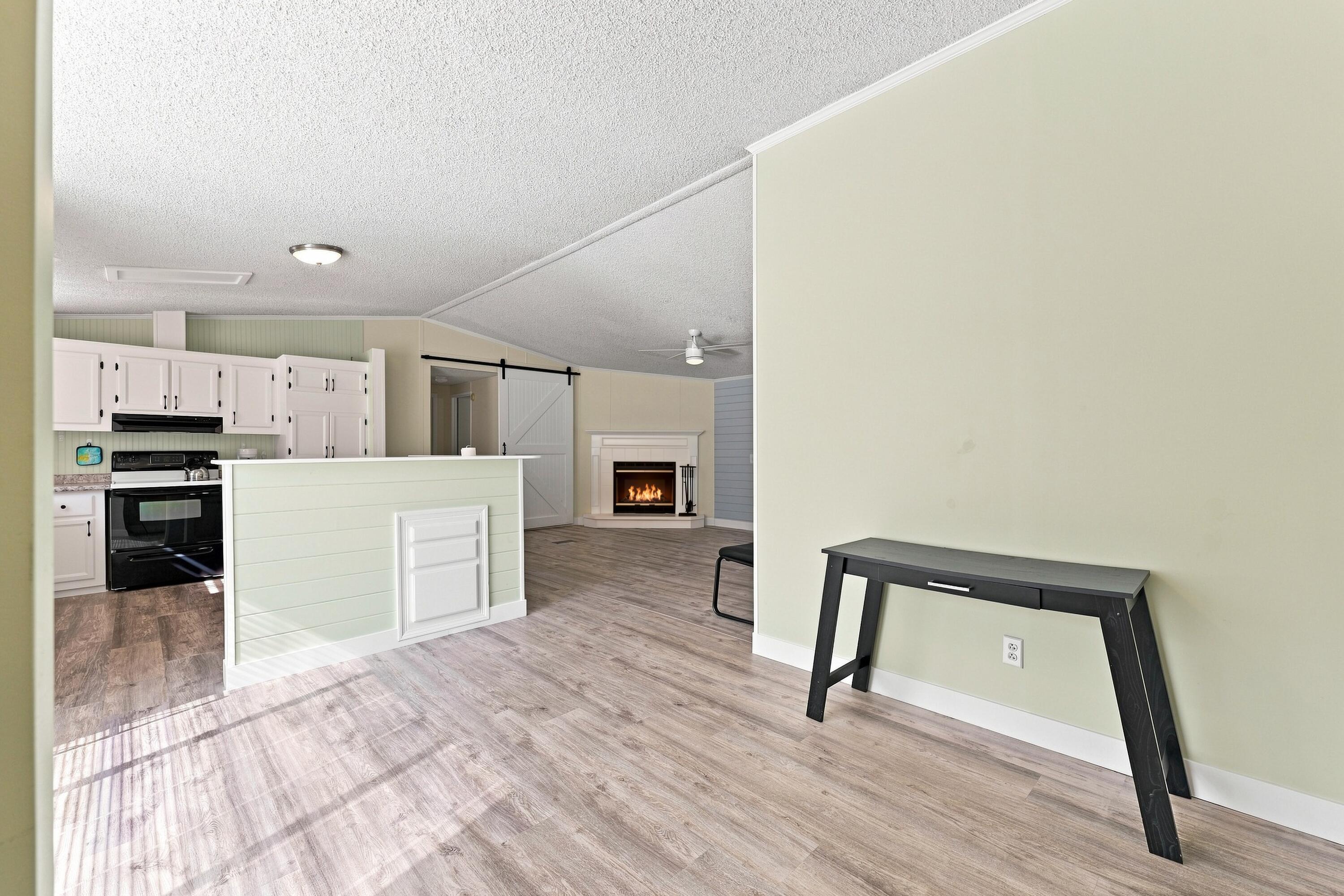 Open-plan kitchen and living area with a pale green island and a fireplace beneath a vaulted ceiling.