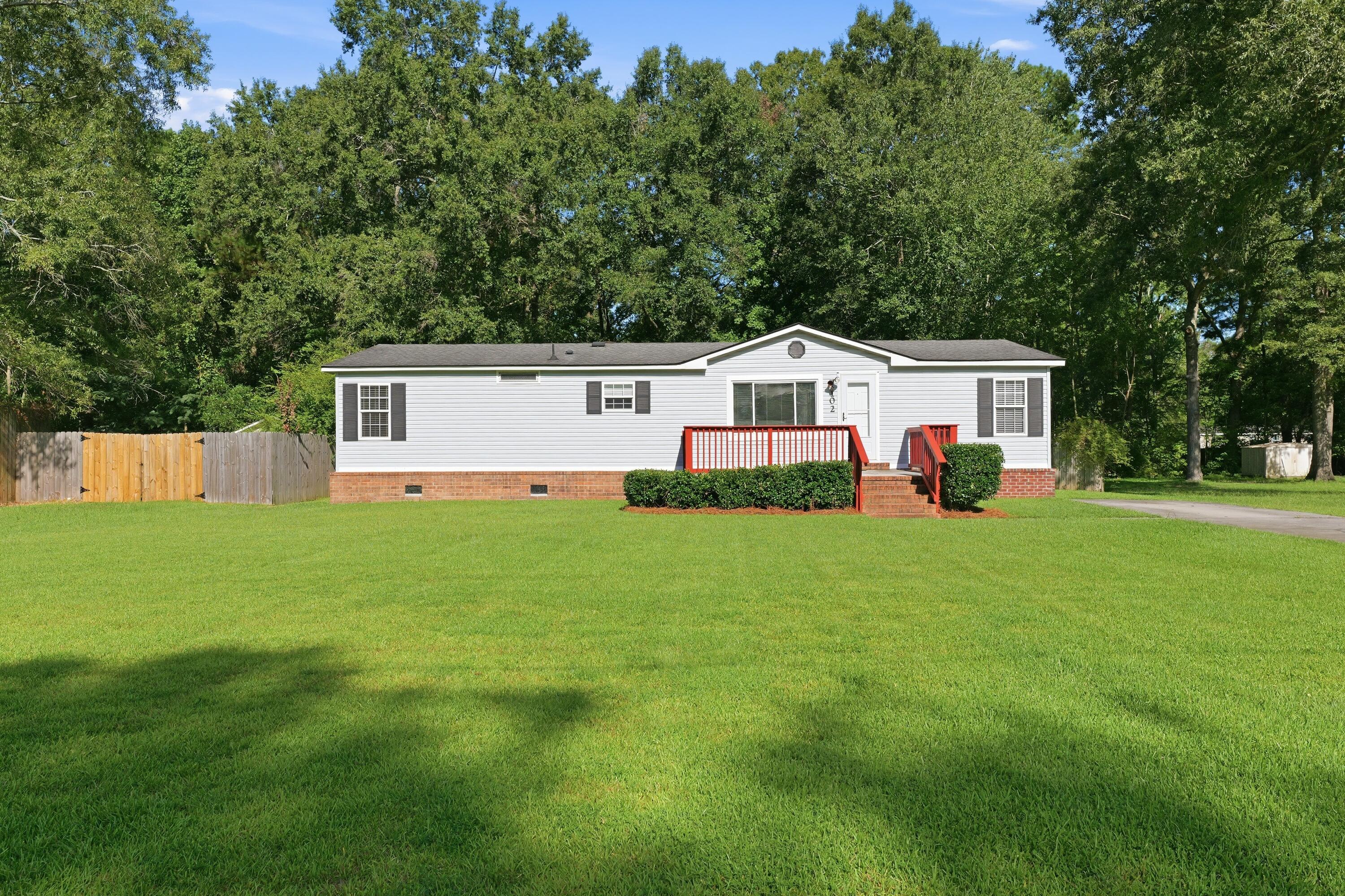 White single-story home with red porch railings and steps, brick foundation, and a broad green lawn.