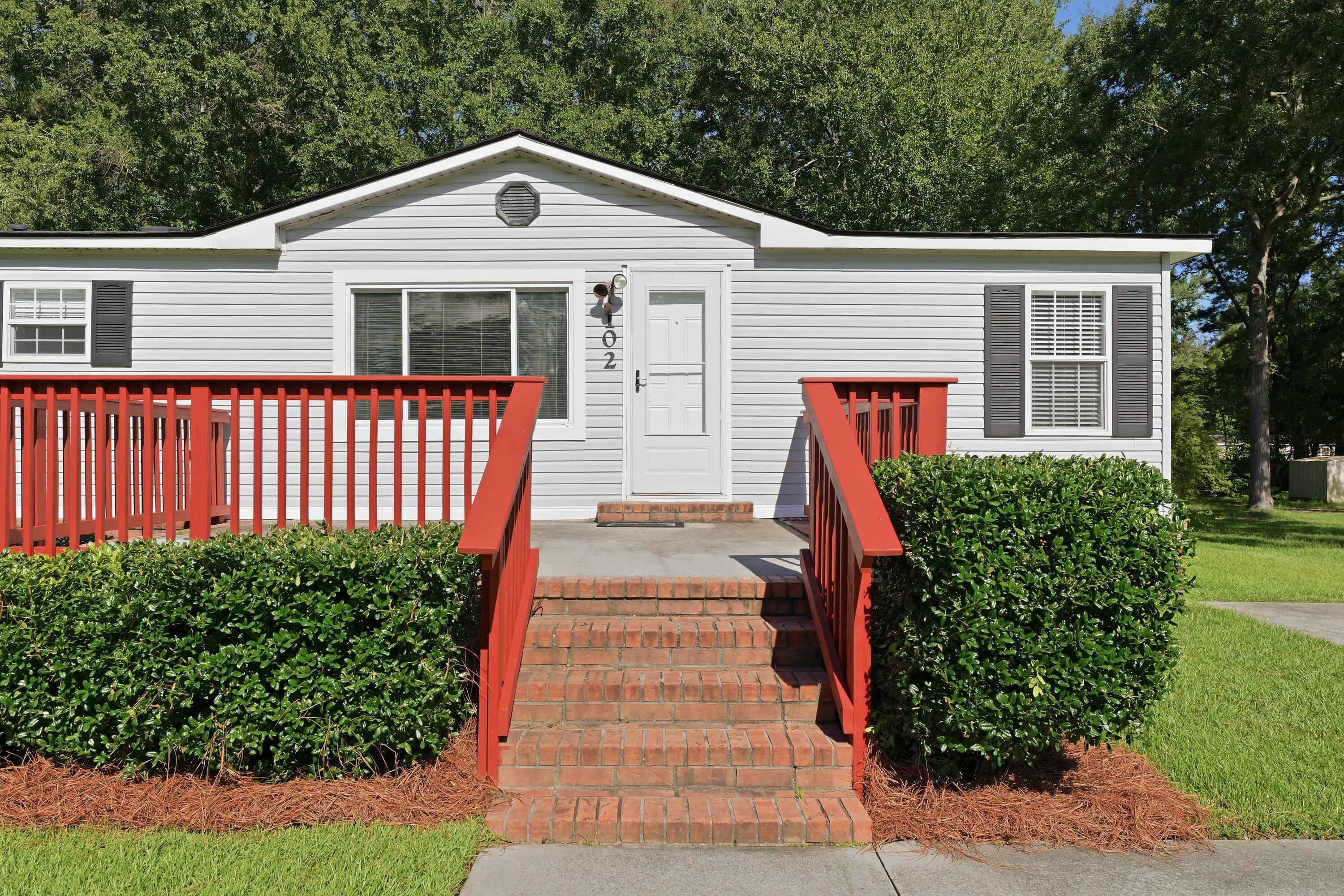 White-sided home with red porch railings and brick steps leading to the front door.