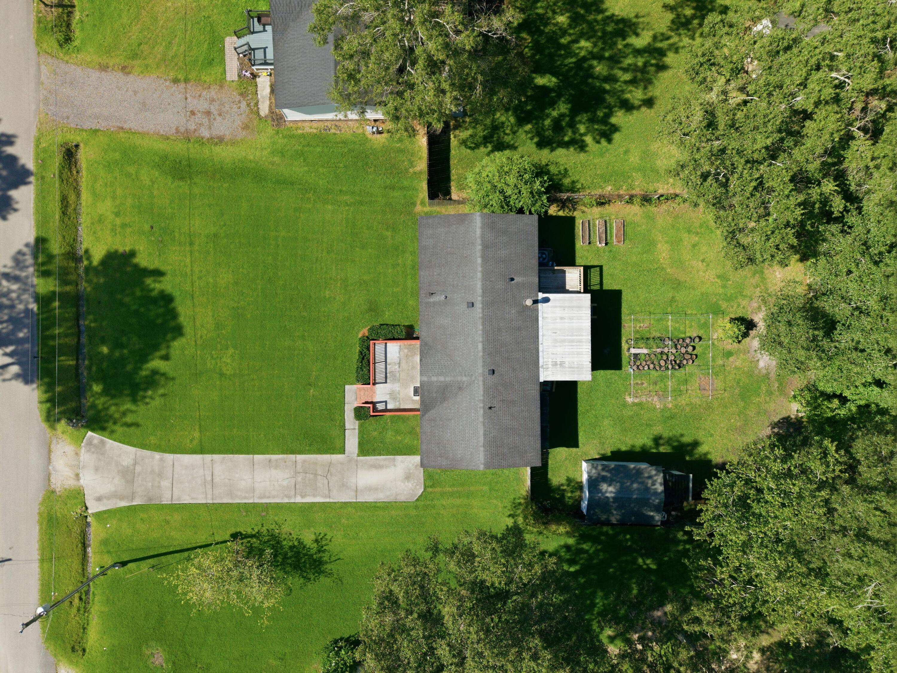 Aerial view of a home with a broad driveway, large lawn, detached shed, and fenced garden beds.