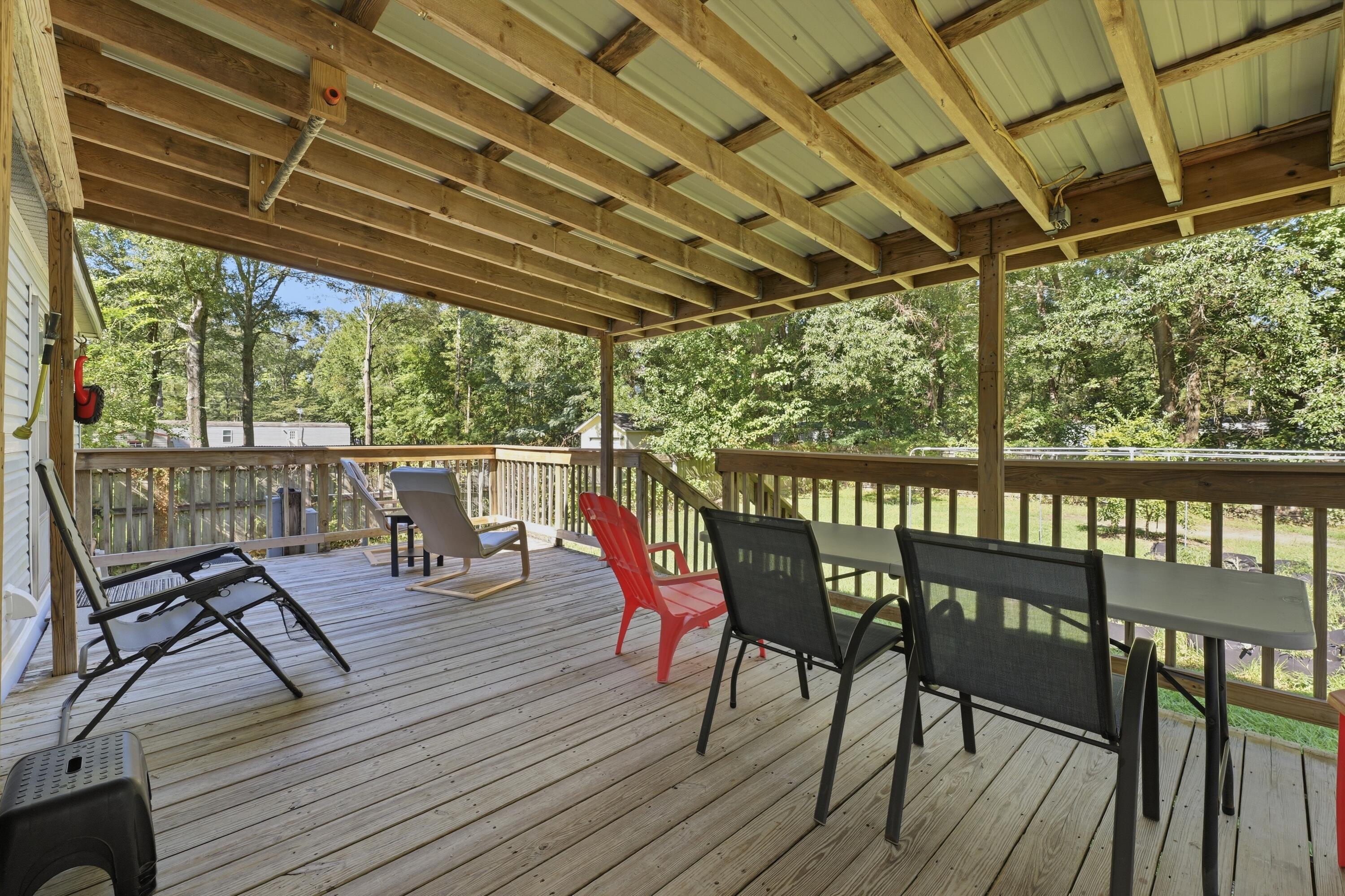 Covered wooden deck with exposed beams, outdoor seating, and a leafy yard beyond the railing.