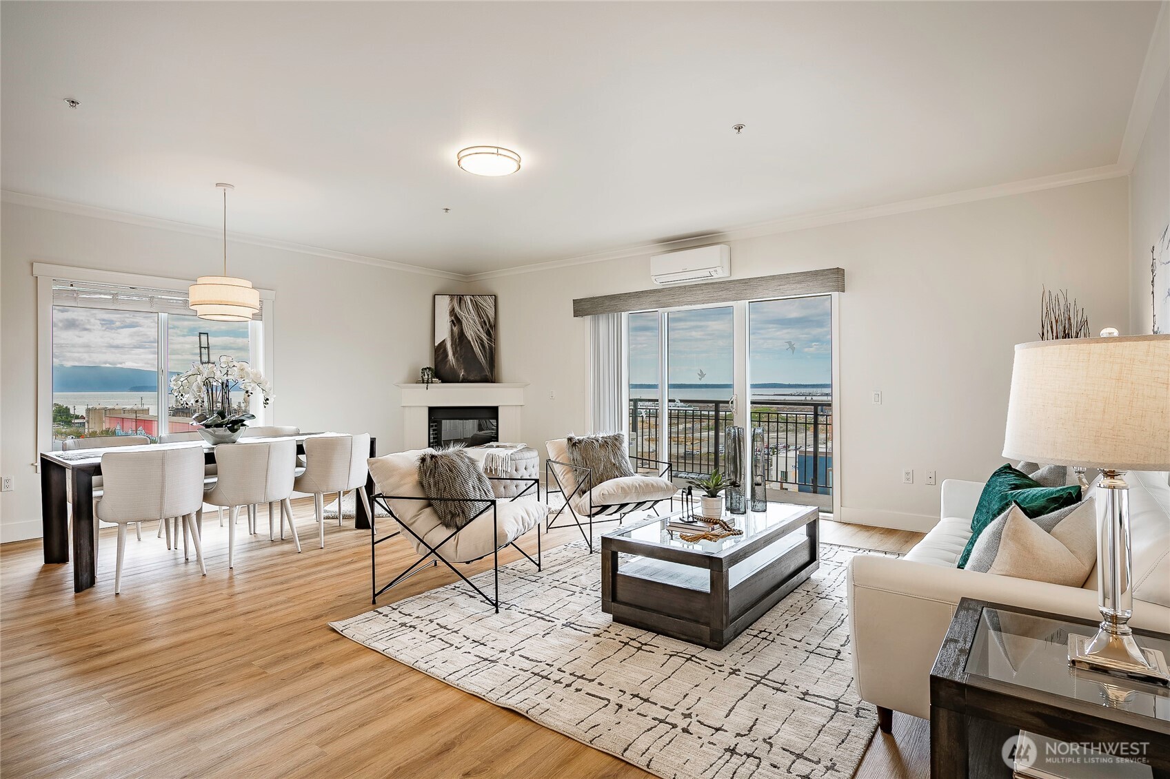 Furnished living and dining room with a fireplace and water views through large windows.