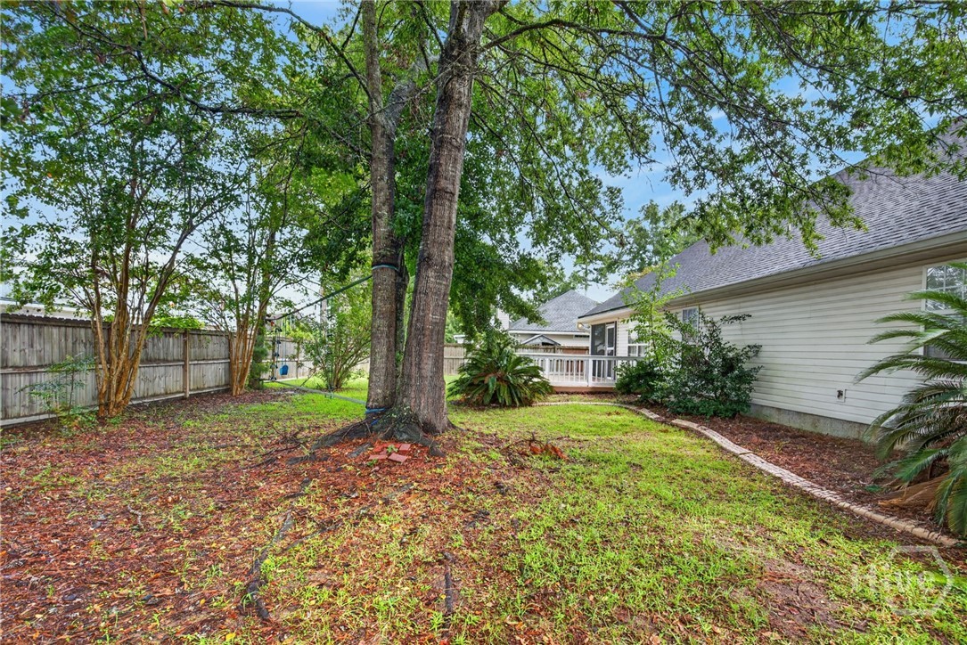 Backyard with mature shade trees, a grassy lawn, and a raised deck beside the house.