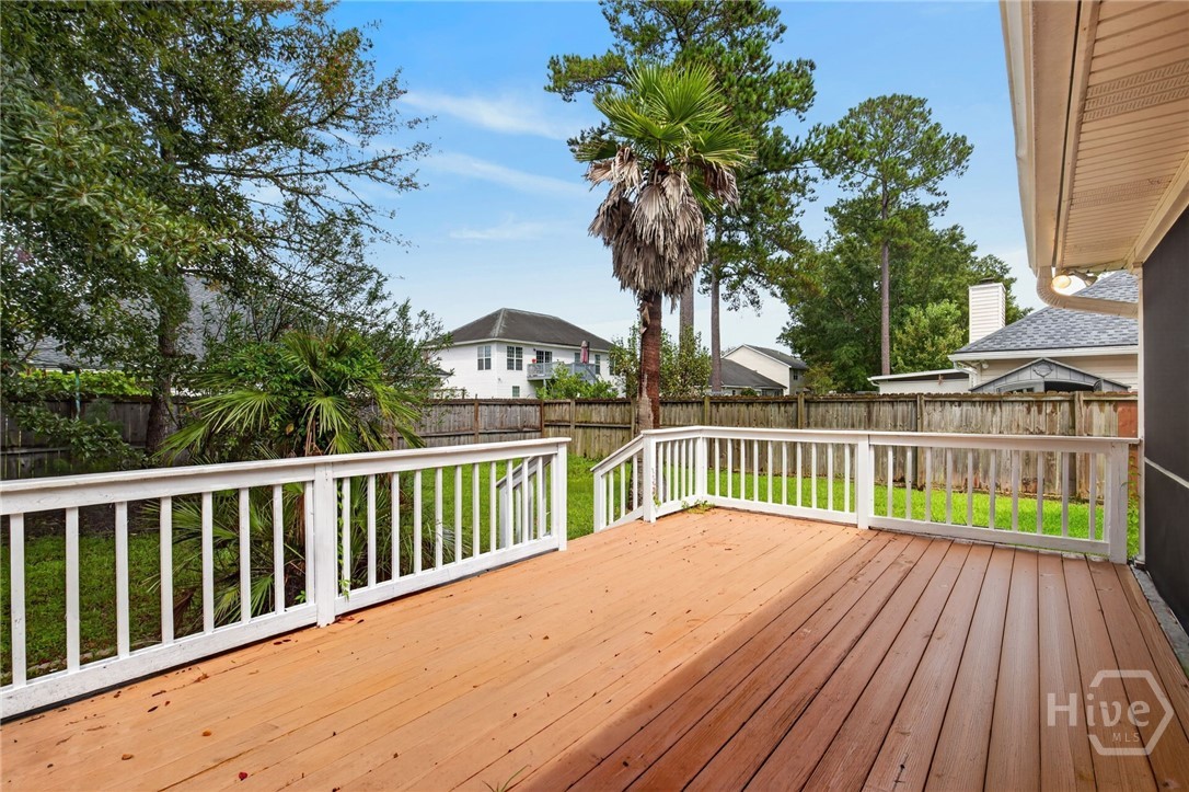 Wooden backyard deck with white railings overlooking a fenced lawn and mature palm trees.