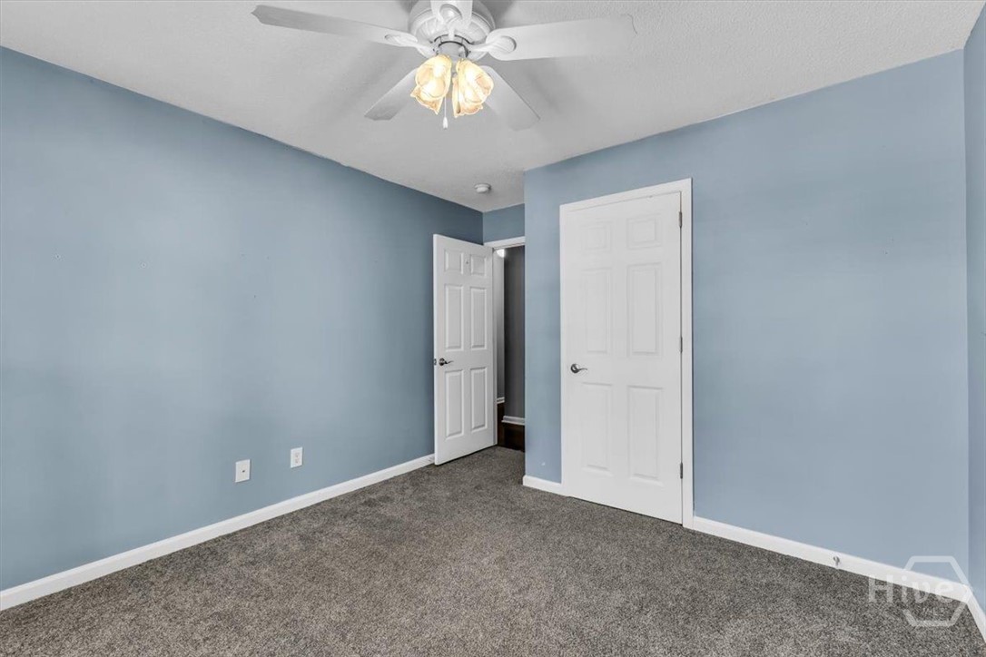 Empty blue-walled room with gray carpet, ceiling fan, and two white doors.