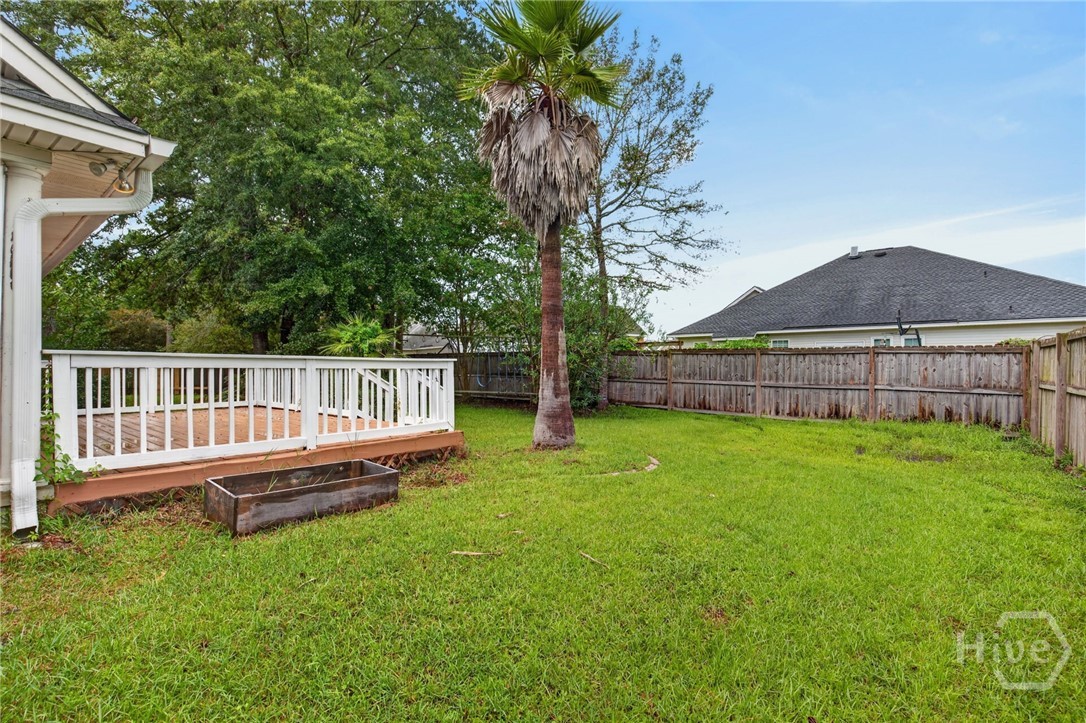 Fenced backyard with a palm tree, broad lawn, and small raised deck with white railings.
