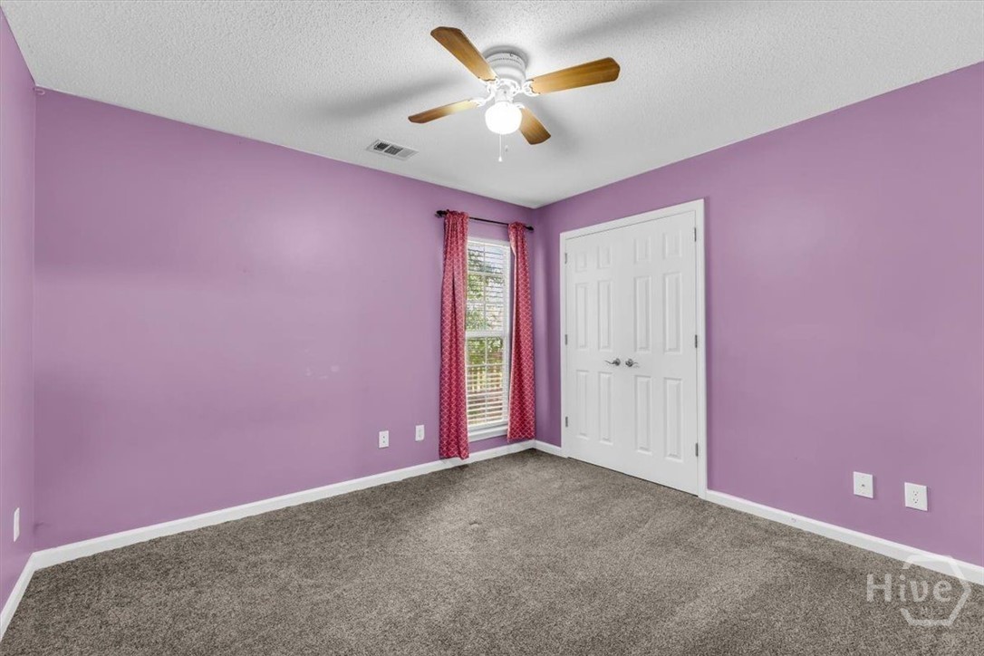 Empty bedroom with lavender walls, gray carpet, red curtains, and white double closet doors.