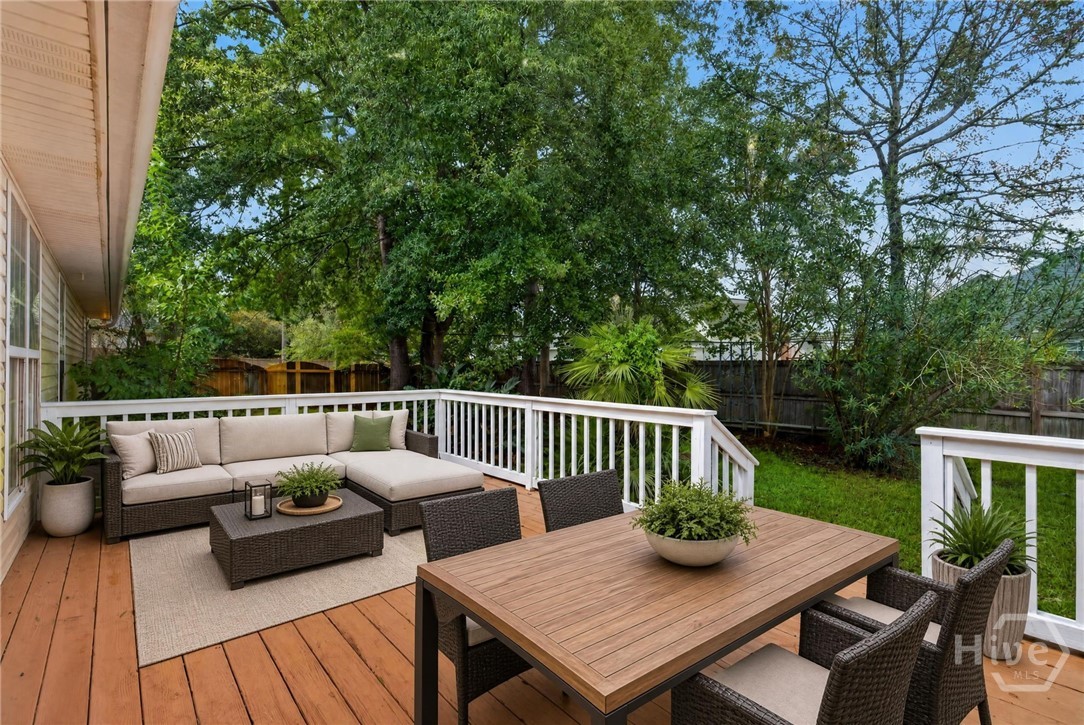Furnished wooden deck with lounge seating and dining table overlooking a leafy fenced yard.