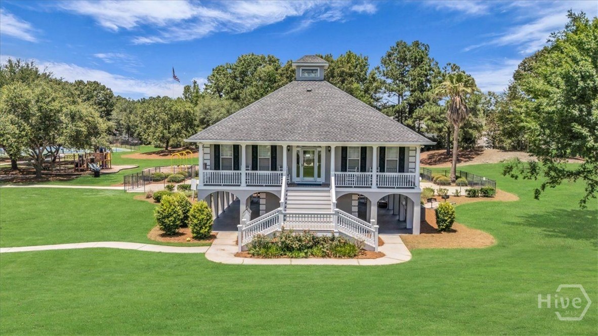 Raised home with a broad front porch and central staircase, surrounded by a green lawn and mature trees.