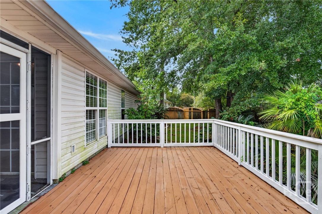Wooden deck with white railings beside the house, overlooking a leafy fenced backyard.