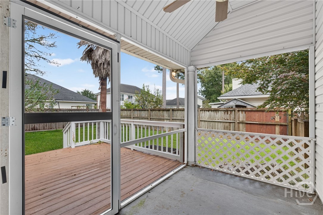 Covered rear porch opening onto a wooden deck and fenced backyard.