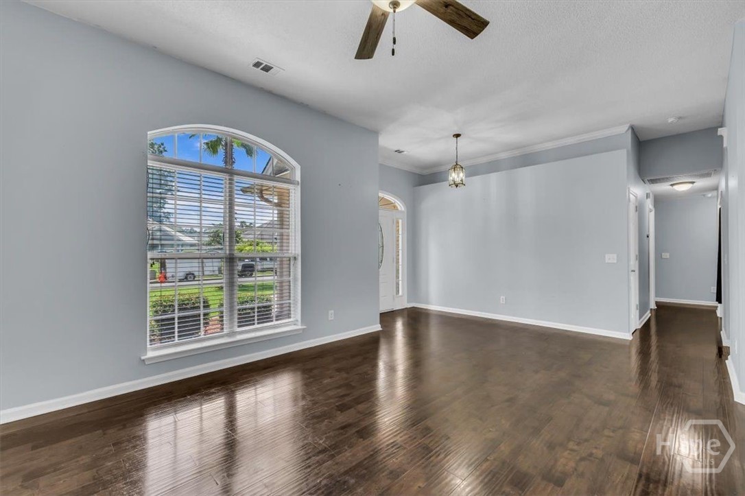 Empty living area with glossy wood floors and a large arched window with blinds.
