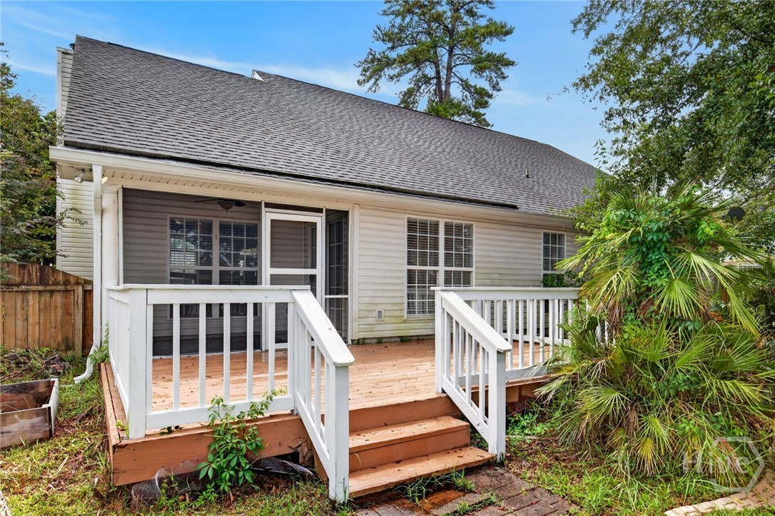 Rear of a gray-sided house with a raised wooden deck, white railings, and surrounding trees.