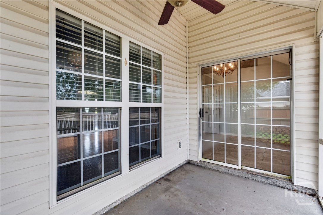 Covered patio with a concrete floor, large divided-pane windows, sliding glass door, and ceiling fan.