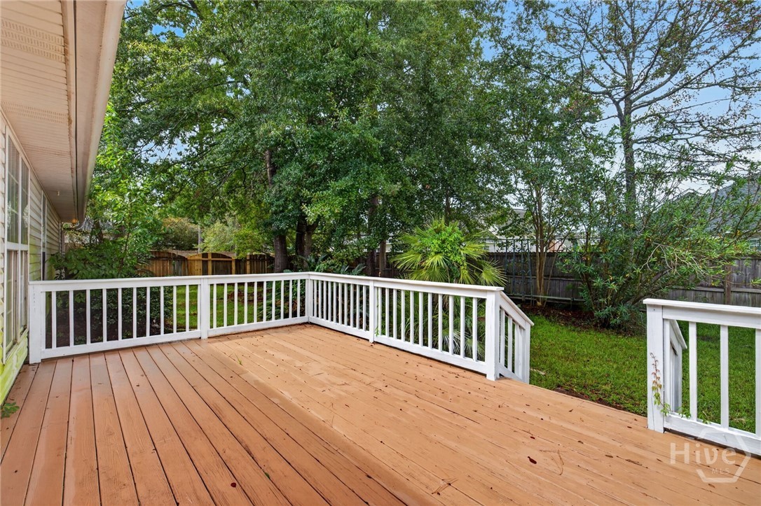 Wooden backyard deck with white railings overlooking a leafy, fenced yard.
