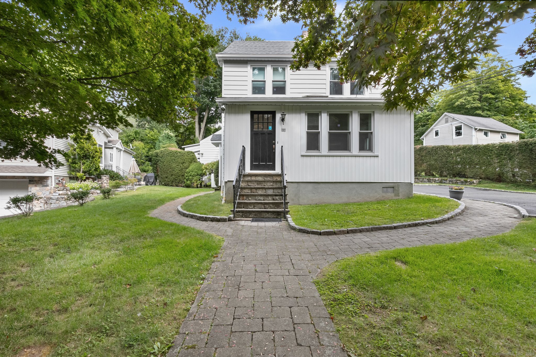 White two-story house with a black front door and curved stone walkway through the lawn.