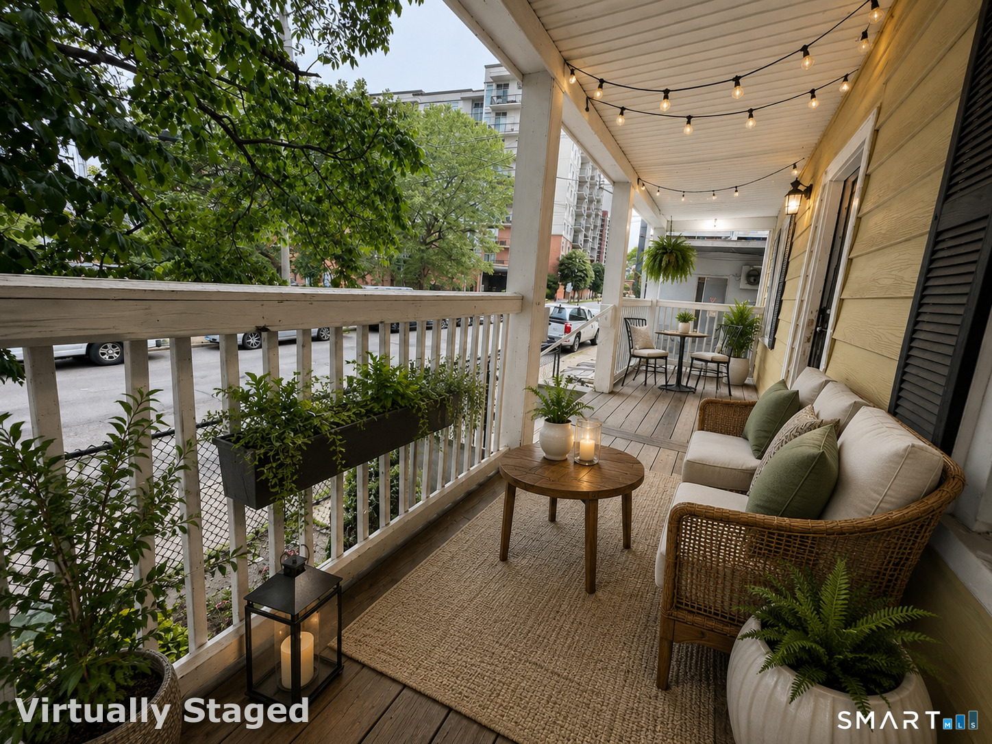 Covered porch with wicker seating, potted plants, a woven rug, and glowing string lights.