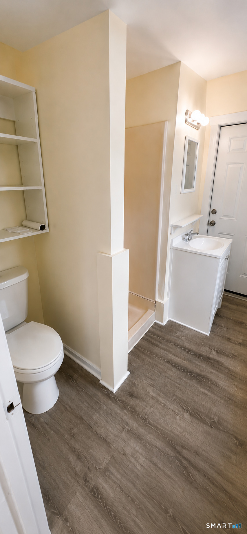 Bathroom with a toilet, open shelving, white vanity, and wood-look flooring.