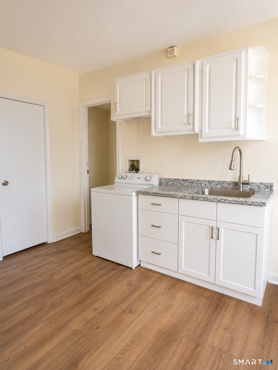 Kitchen with white cabinets, granite countertop, stainless-steel sink, and washer.