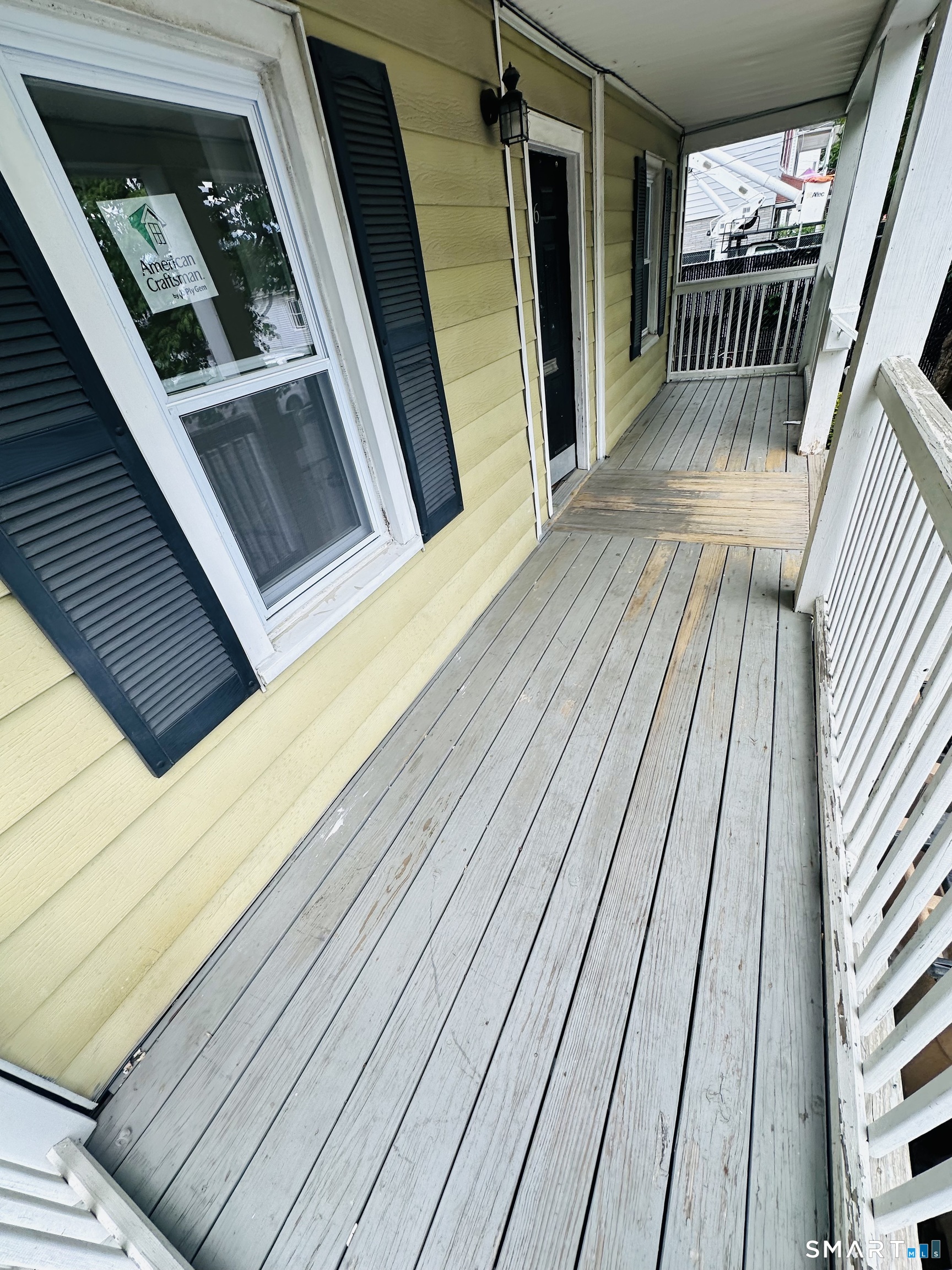 Weathered wooden porch leading to a black entry door on a pale yellow-sided home.