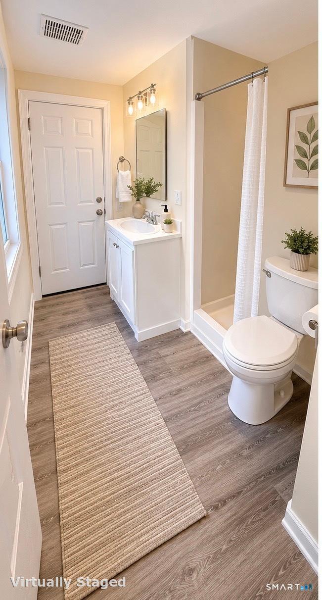 Bathroom with a white vanity, curtained tub and shower, and long beige runner on gray wood-look flooring.