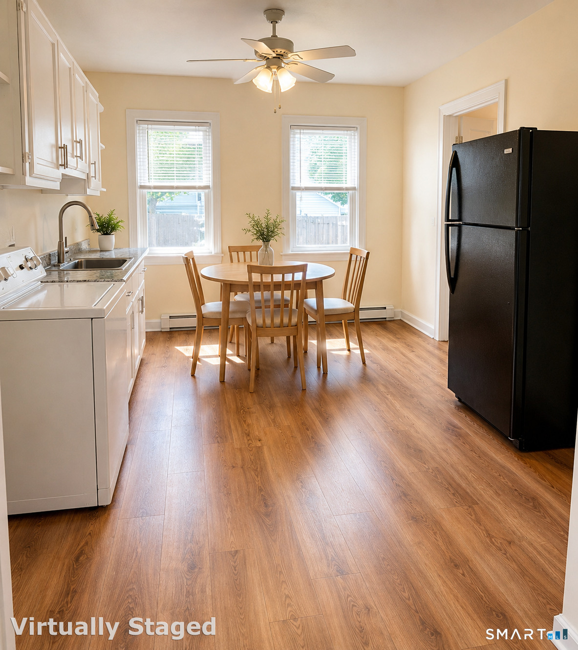Kitchen with a round dining table between two windows, white cabinets, and wood-look flooring.