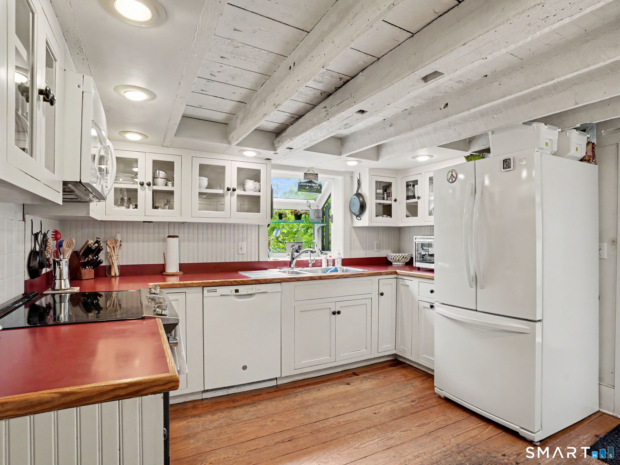 Kitchen with white cabinetry, red countertops, exposed ceiling beams, and wood plank flooring.