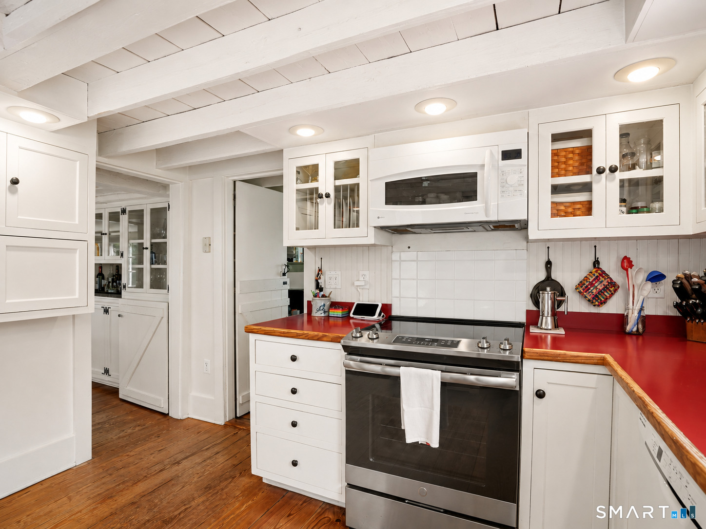 Kitchen with red countertops, white cabinetry, exposed ceiling beams, and a stainless-steel range.