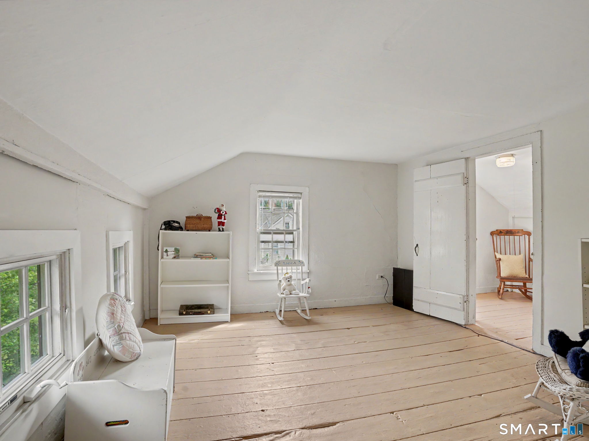 Attic room with a sloped ceiling, wide-plank floors, white shelving, and rocking chairs.