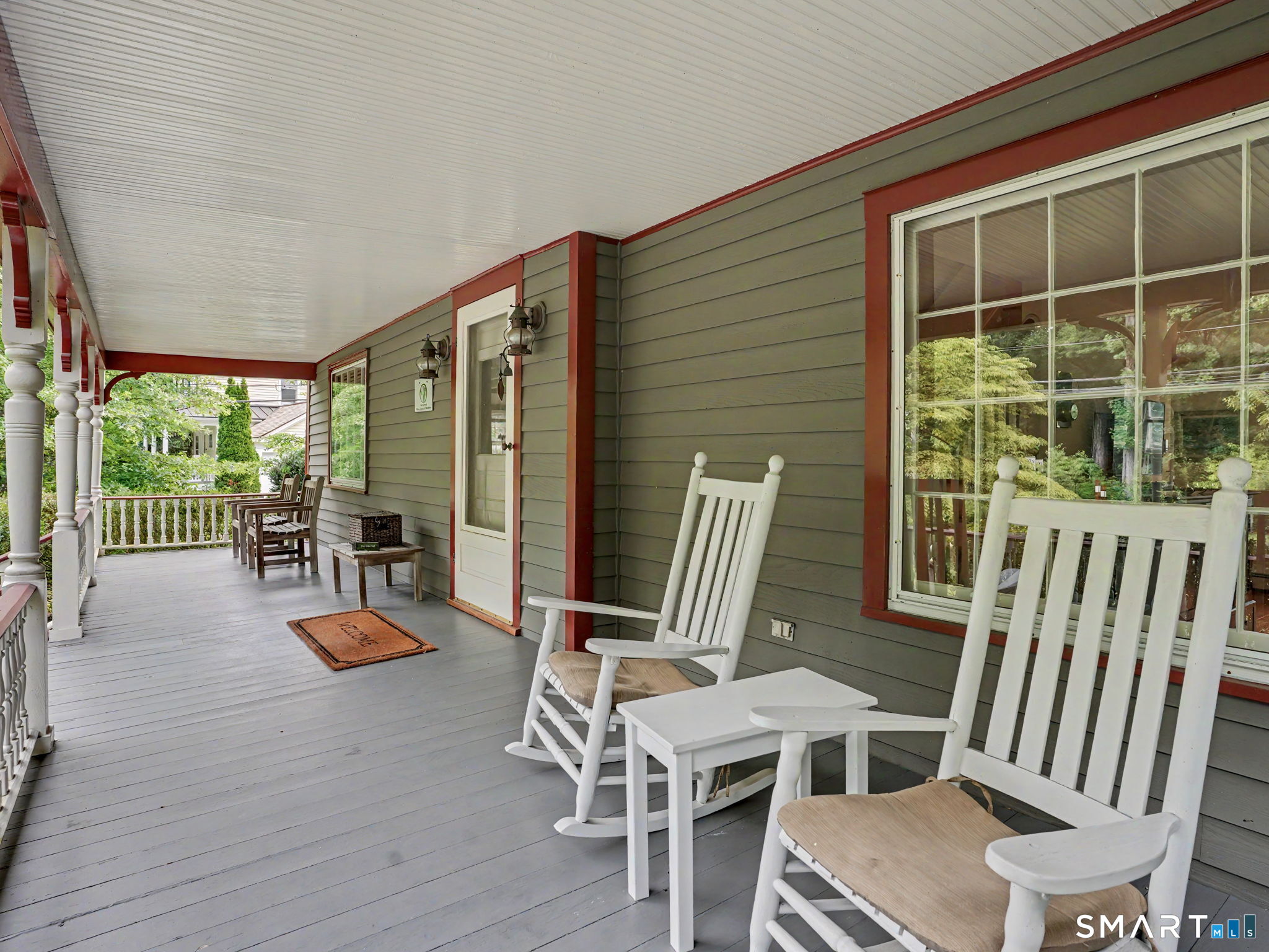 Covered front porch with white rocking chairs, gray siding, and red trim.