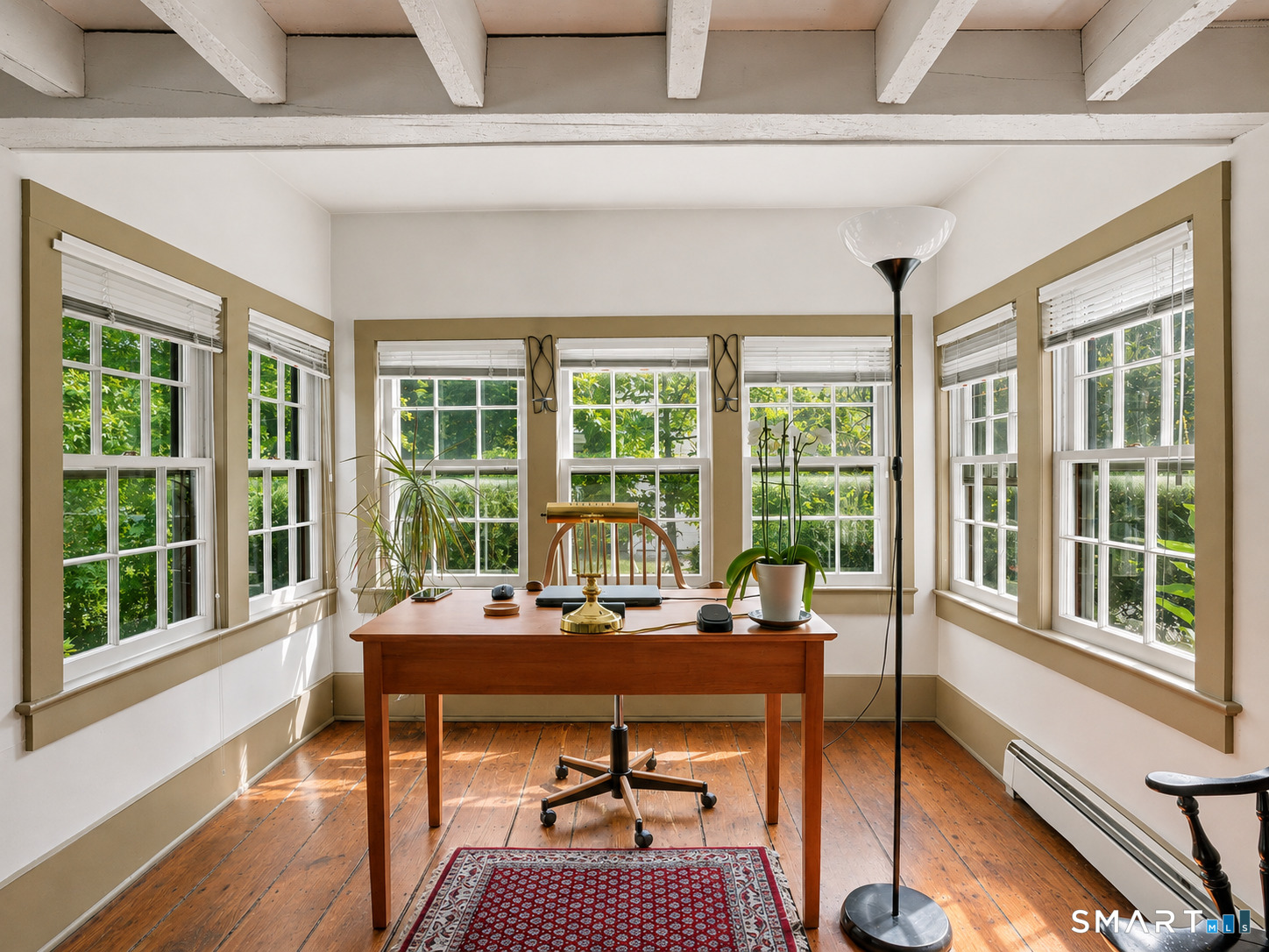 Bright home office with a wooden desk, exposed beams, and windows overlooking greenery.