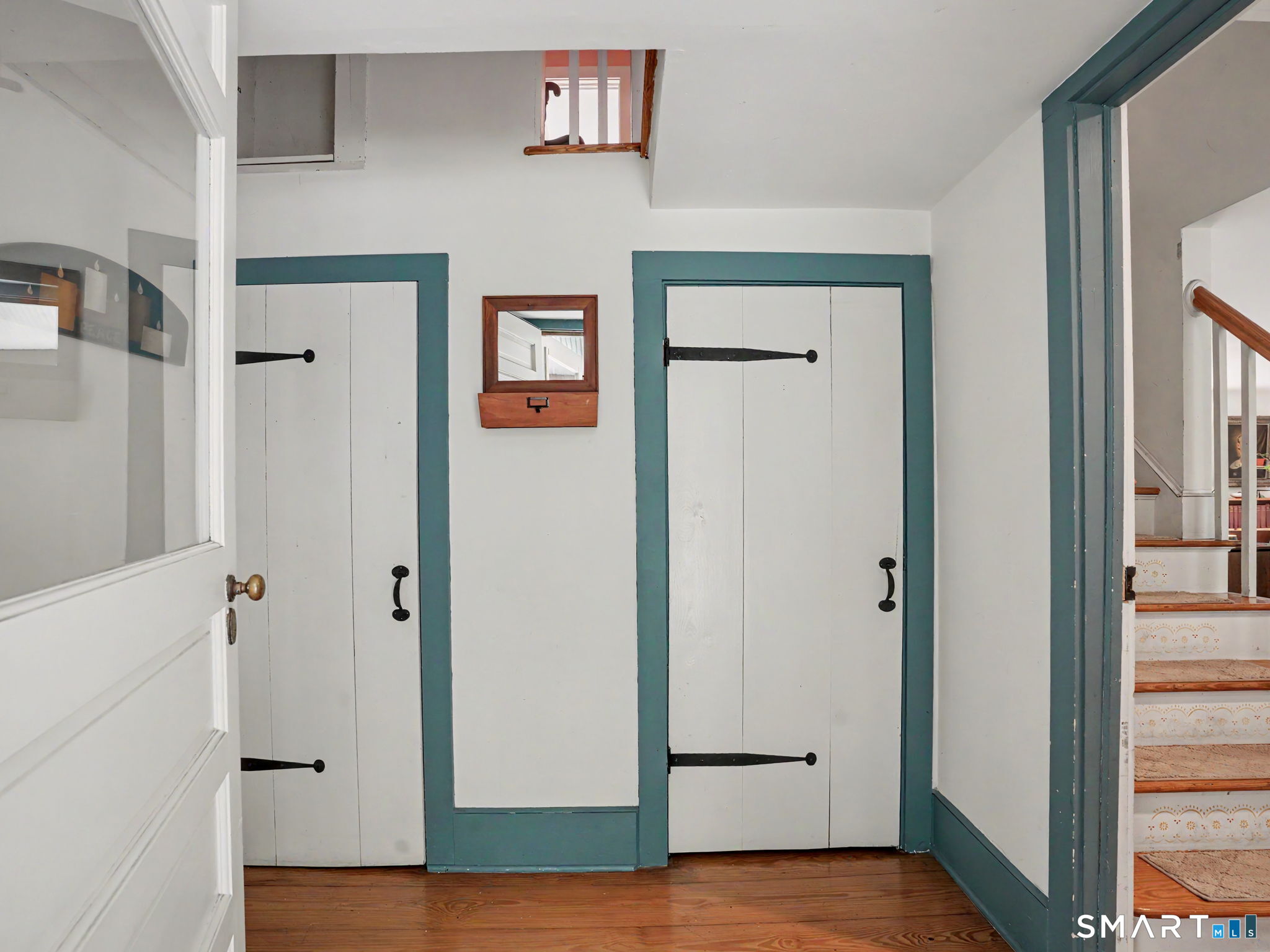 Hallway with teal-trimmed white doors, hardwood floors, and a staircase.