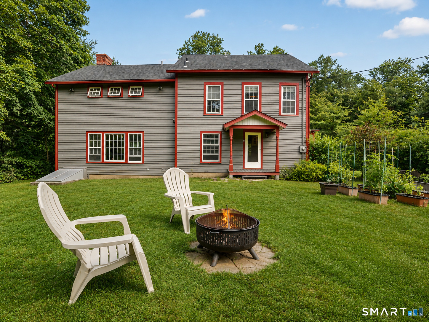 Rear of a gray two-story home with red trim, lawn chairs, and a fire pit.