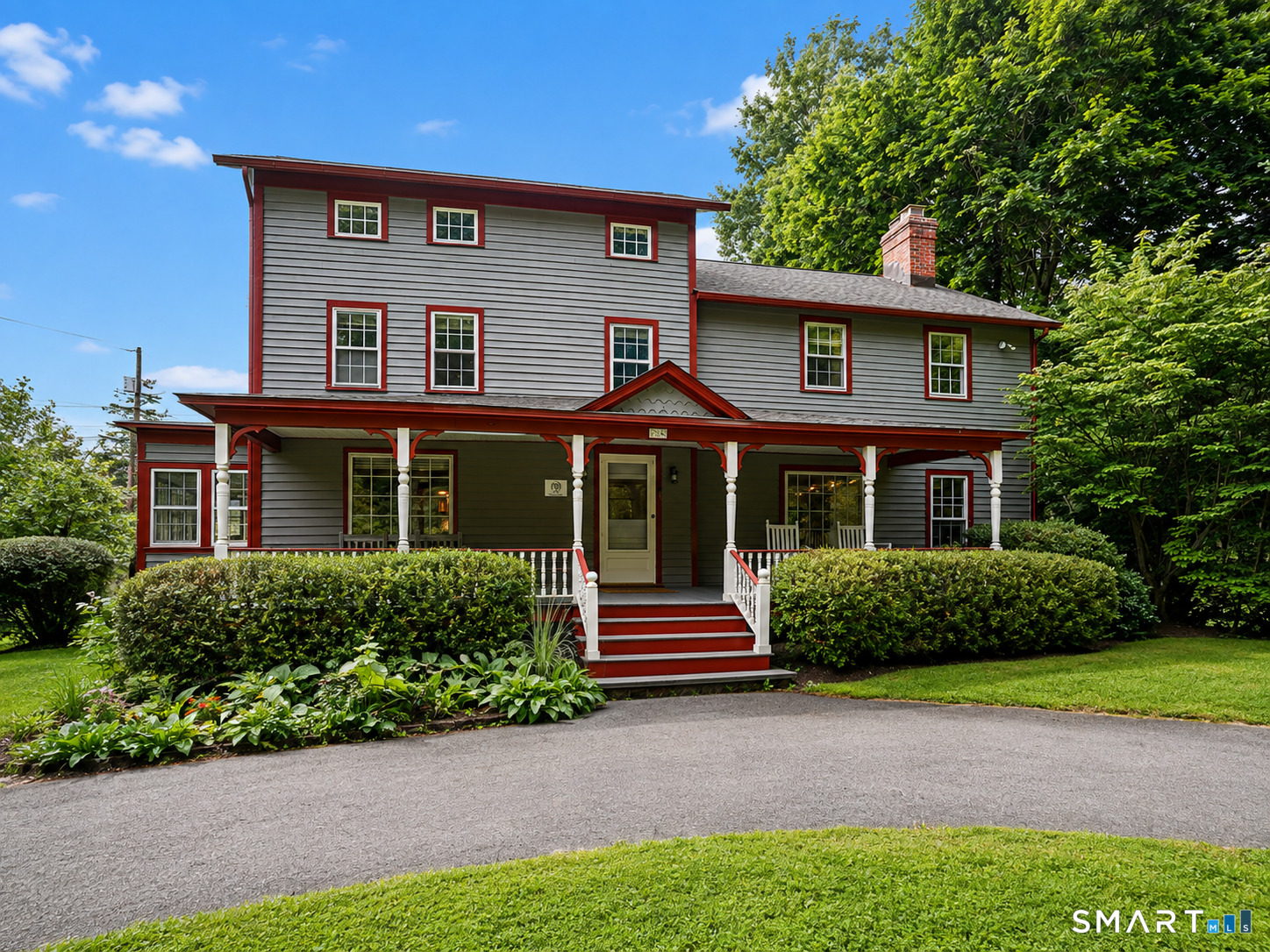 Gray two-story house with red trim, a covered porch, red steps, and landscaped gardens.