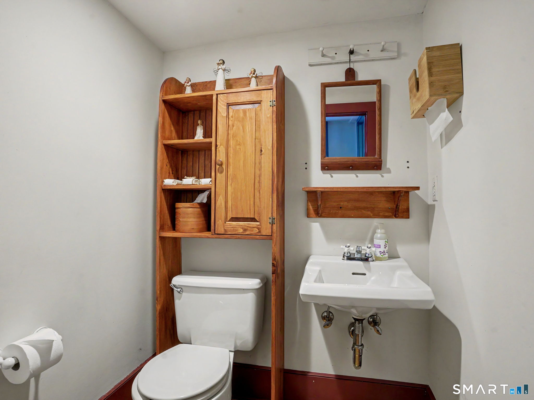Bathroom with a white toilet, wall-mounted sink, and wooden shelving around the toilet.