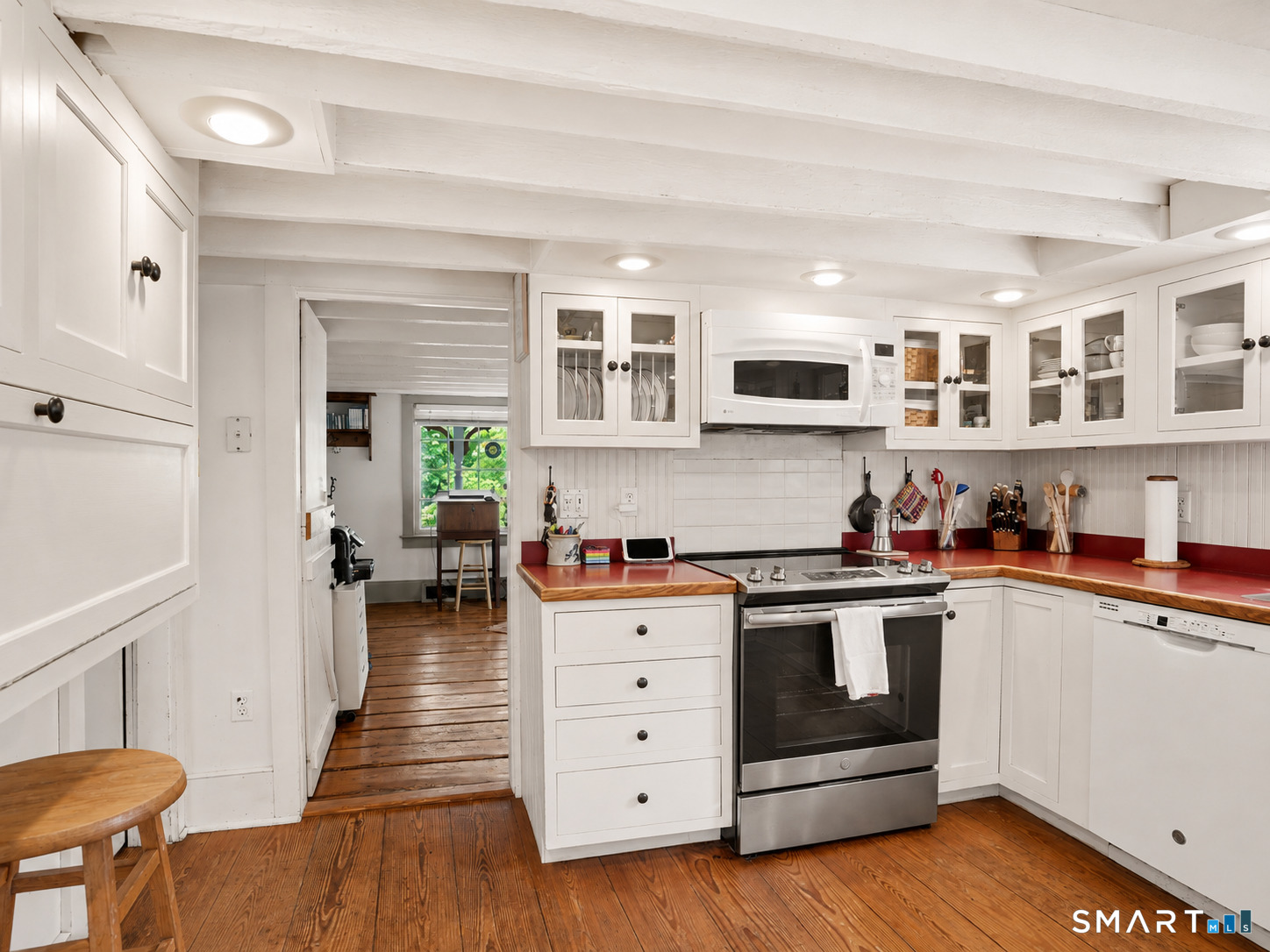 Kitchen with white cabinets, red countertops, stainless steel appliances, and warm wood plank floors.
