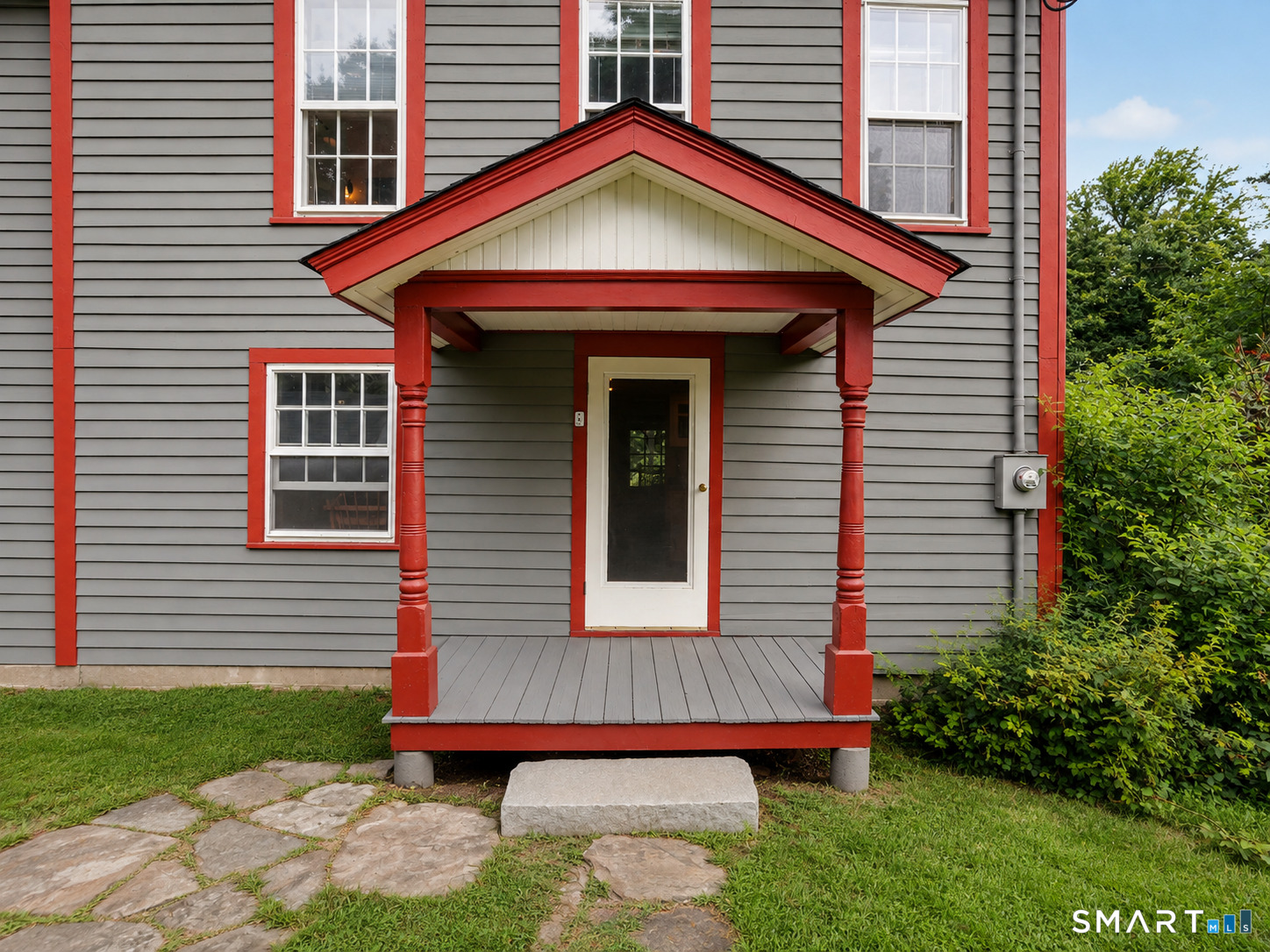 House entrance with a red-trimmed covered porch, gray siding, and stone walkway.