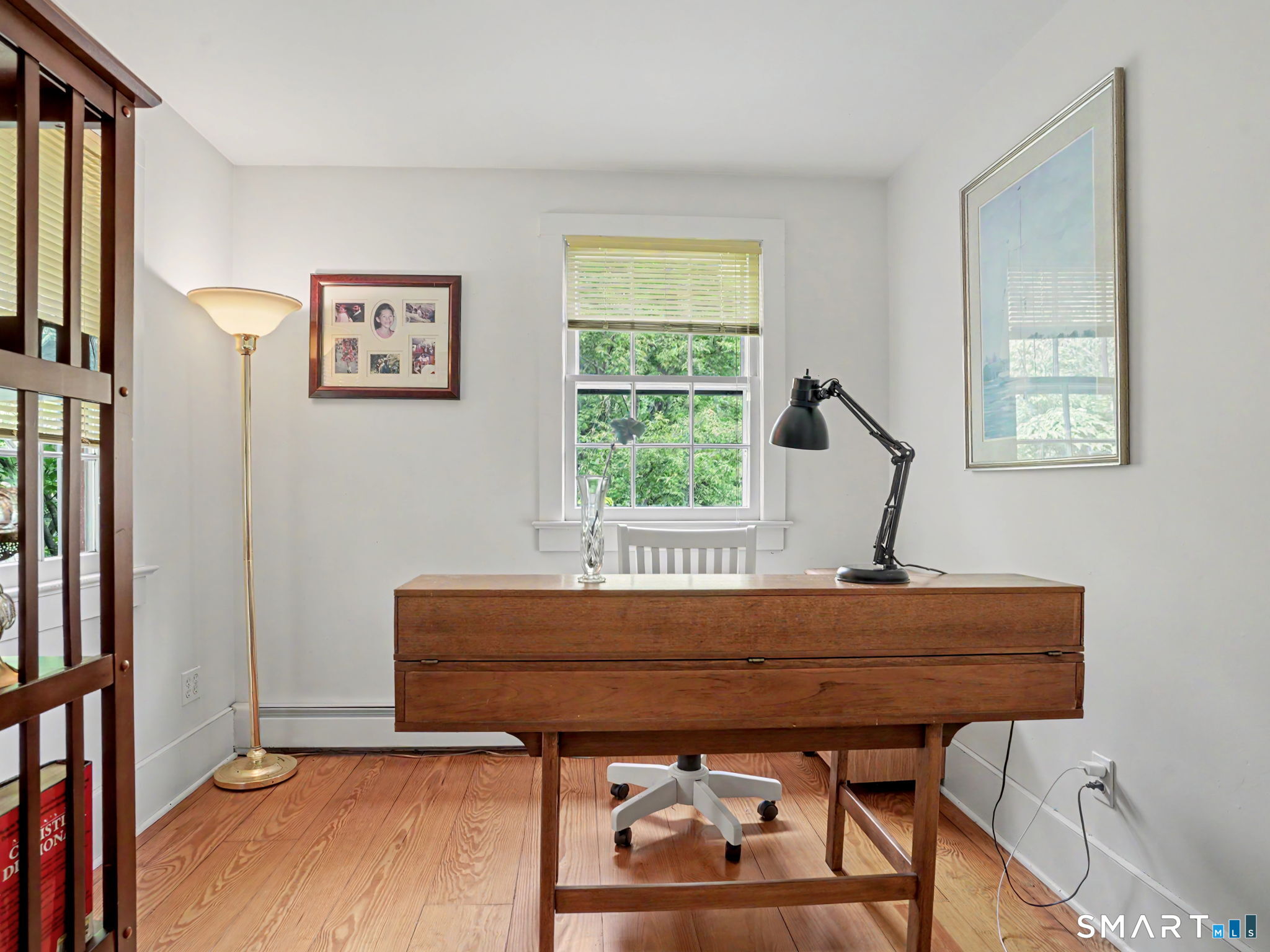 Home office with a wooden desk, hardwood floors, and windows overlooking greenery.