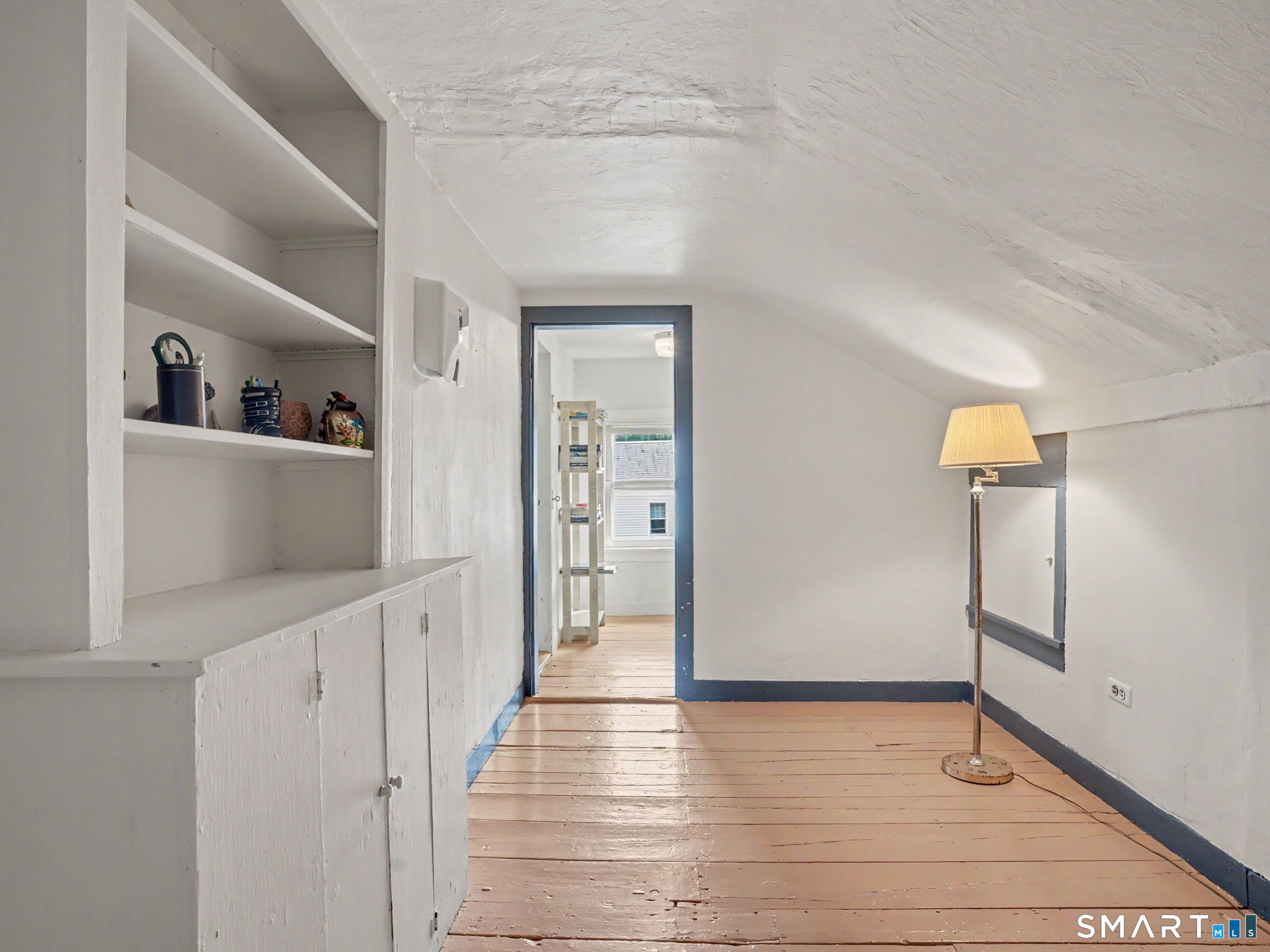 Finished attic room with built-in shelves, sloped ceiling, blue trim, and wide painted wood floors.