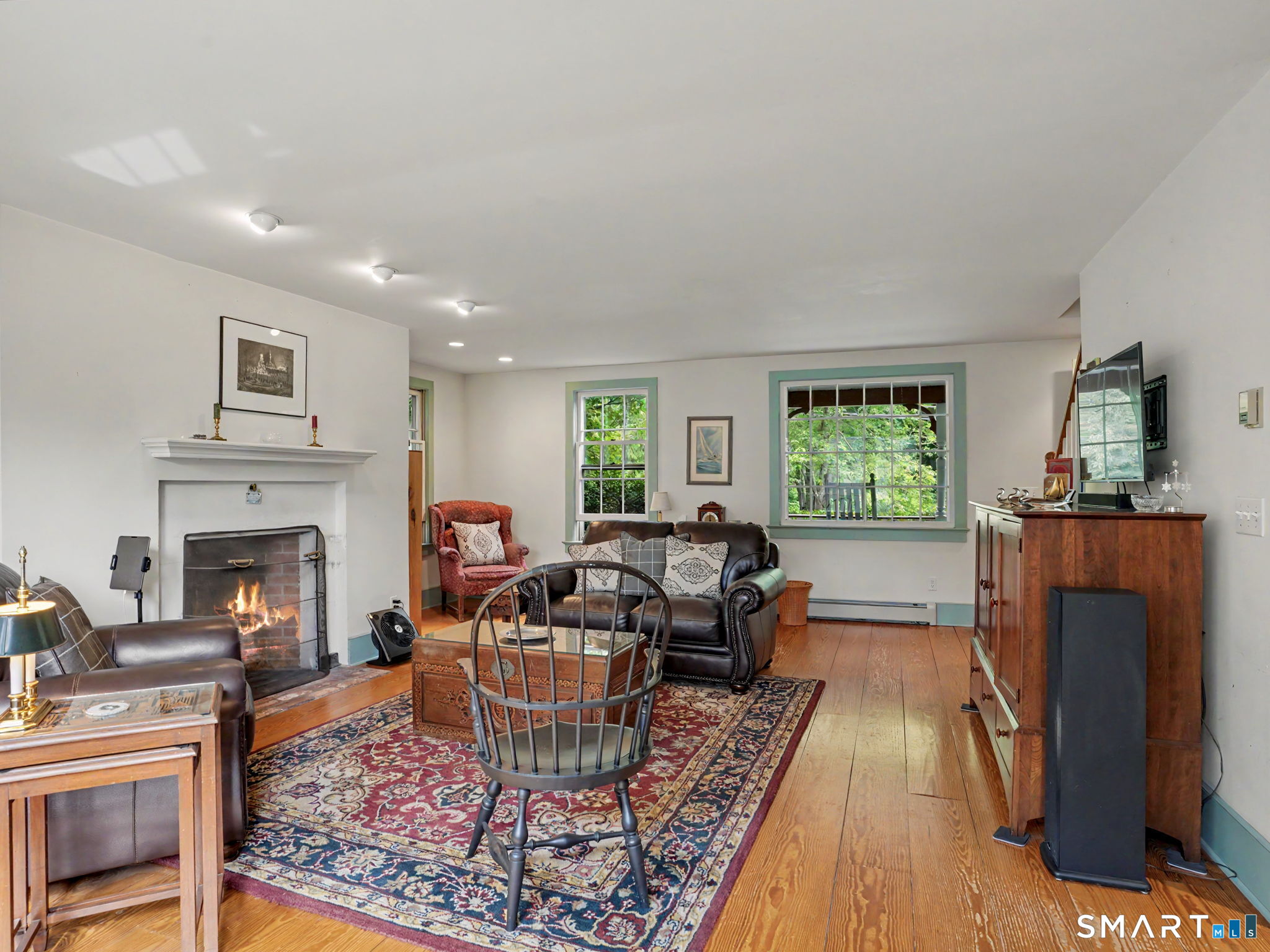 Furnished living room with a wood-burning fireplace, patterned rug, and green-trimmed windows.