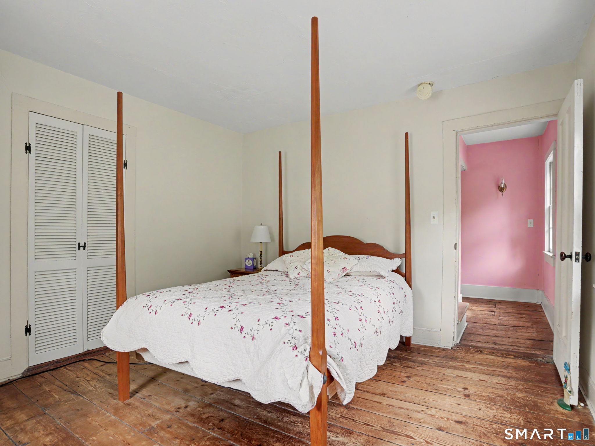 Bedroom with a wooden four-poster bed, floral bedding, and exposed plank floors.
